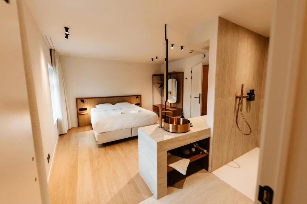 Chambre moderne avec un lit double, un mur en bois, une salle de bain attenante avec douche, un miroir, un meuble en bois, et des lampes encastrées au plafond.