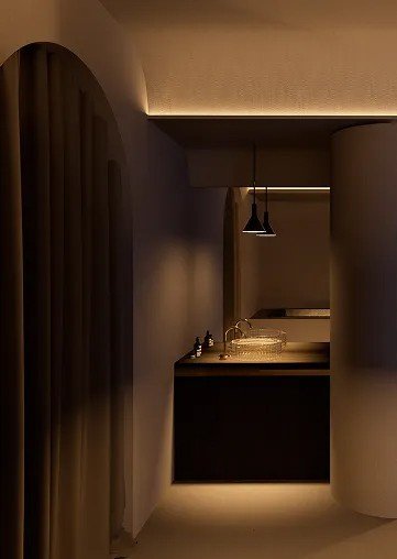 Intérieur d'une pièce moderne avec un coin cuisine, éclairée tamisé, comprenant un îlot de cuisine, un évier, et un éclairage indirect.