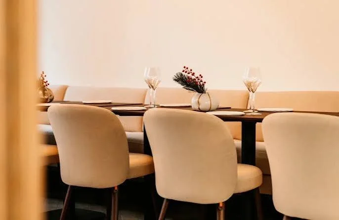 Table de restaurant élégante avec des assiettes, des verres à vin et un vase de fleurs séchées, dans un décor moderne et minimaliste.