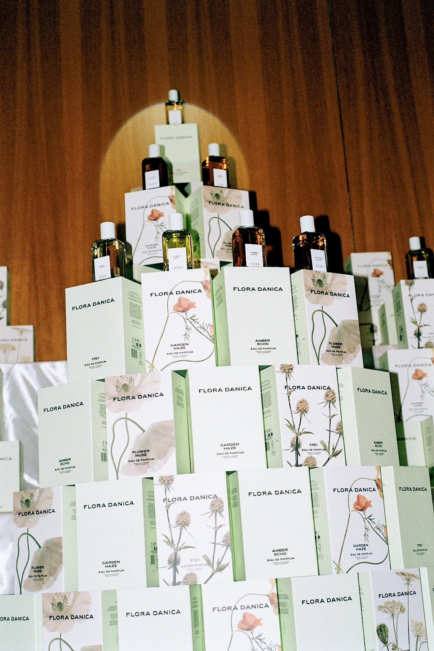 Display of Flora Danica perfume bottles placed on their packaging with botanical illustrations on a wooden background.