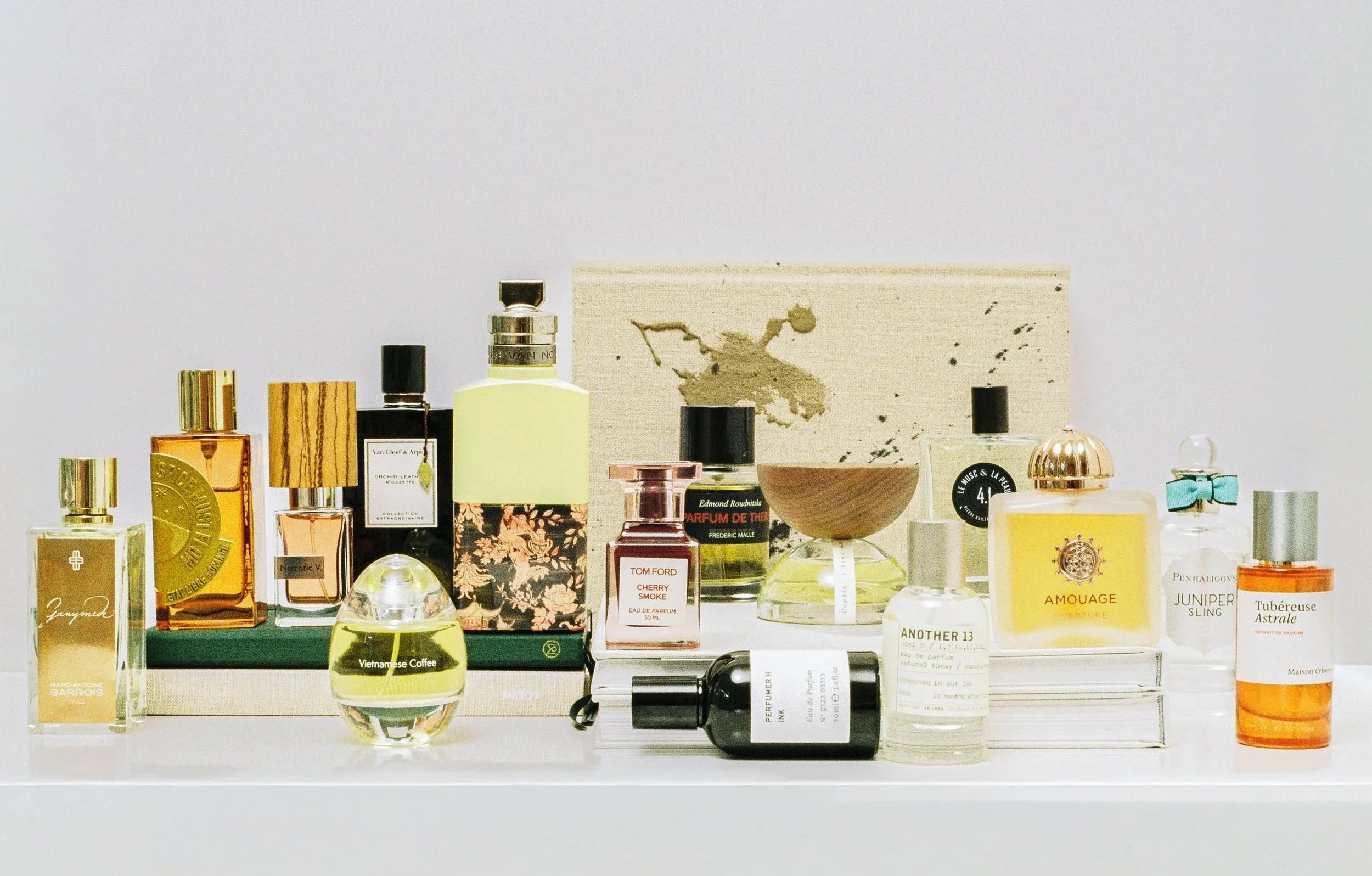 A collection of various perfume bottles arranged on a white shelf with a white background, including brands like Tom Ford, Amouage, and Penhaligon's.