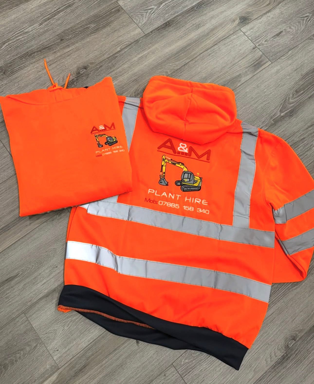 High-visibility orange hi-vis jacket and bag for a plant hire company, with reflective stripes and company logo, lying on a wooden floor.