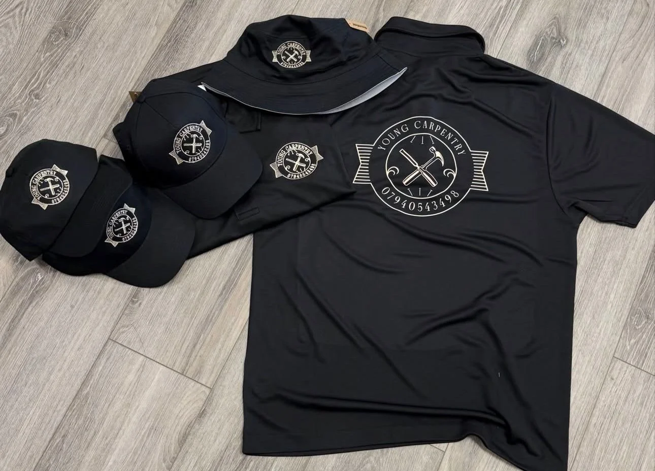 Set of black apparel and accessories with white logo and text for Young Carpentry, including two caps, a long-sleeve shirt, and a short-sleeve shirt, all with the company's logo featuring a hammer and screwdriver.