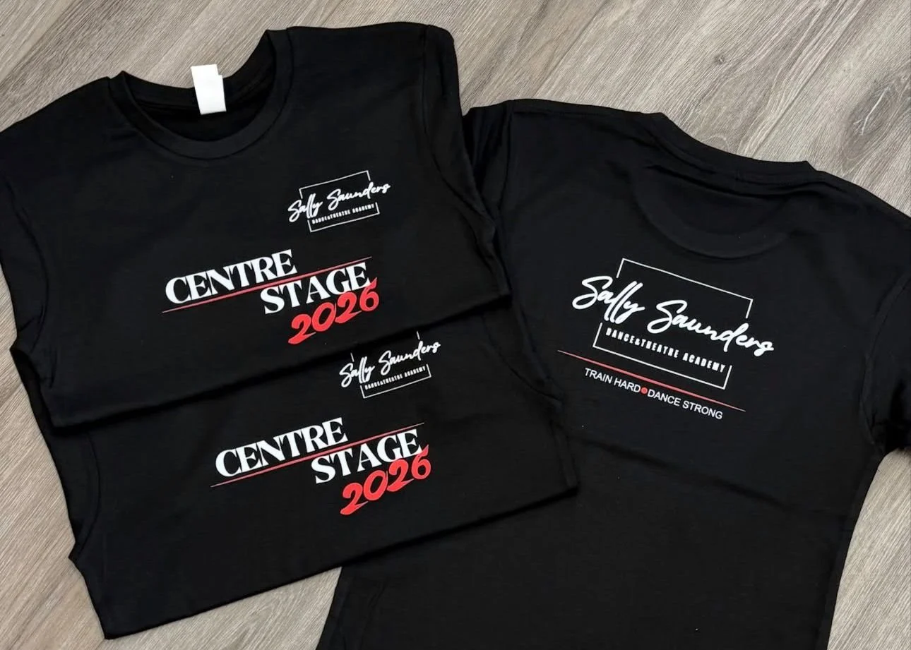 Two black T-shirts with Sally Saunders Dance Company branding; one shows 'Centre Stage 2026' in white and red text, and the other has her name with logos and motivational phrases.