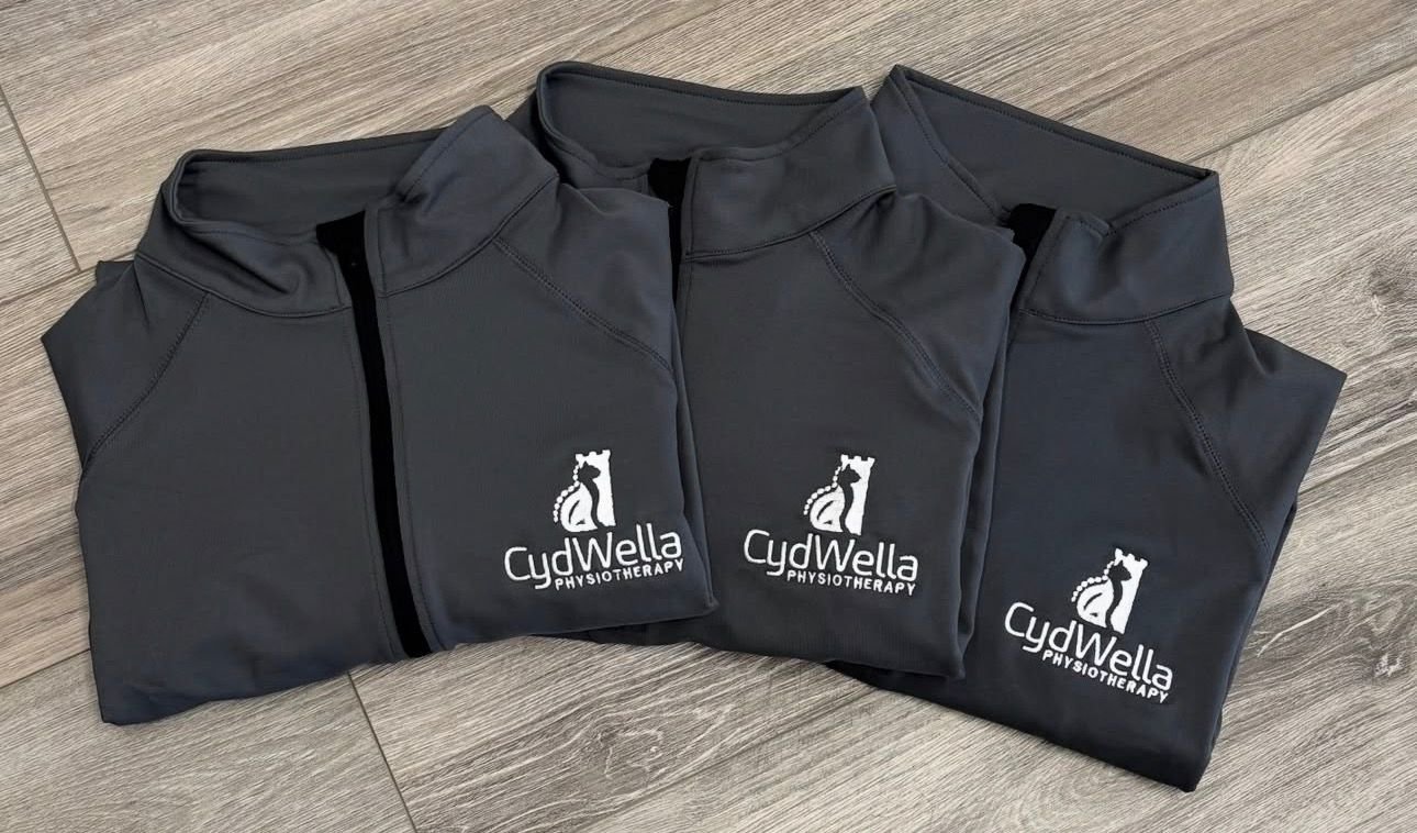Three black CydWella Physiotherapy jackets with logo, laid flat on wooden floor.