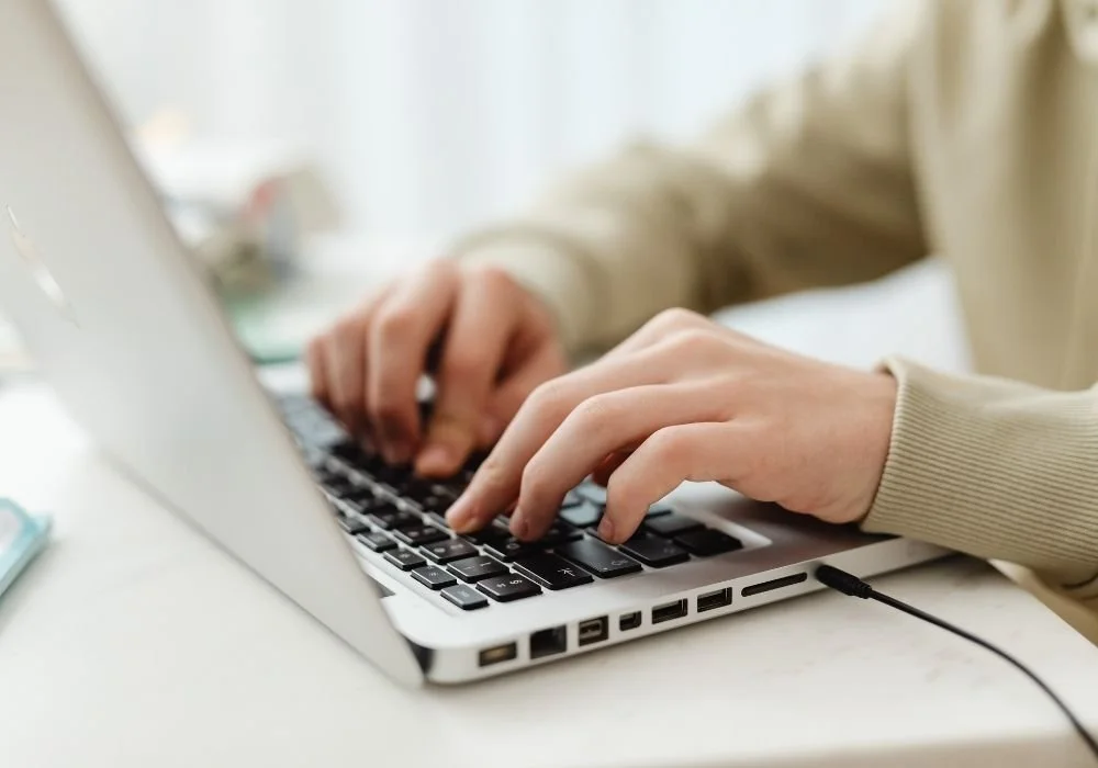 Paul Wogan Therapy. Person typing on a silver laptop keyboard at a desk.