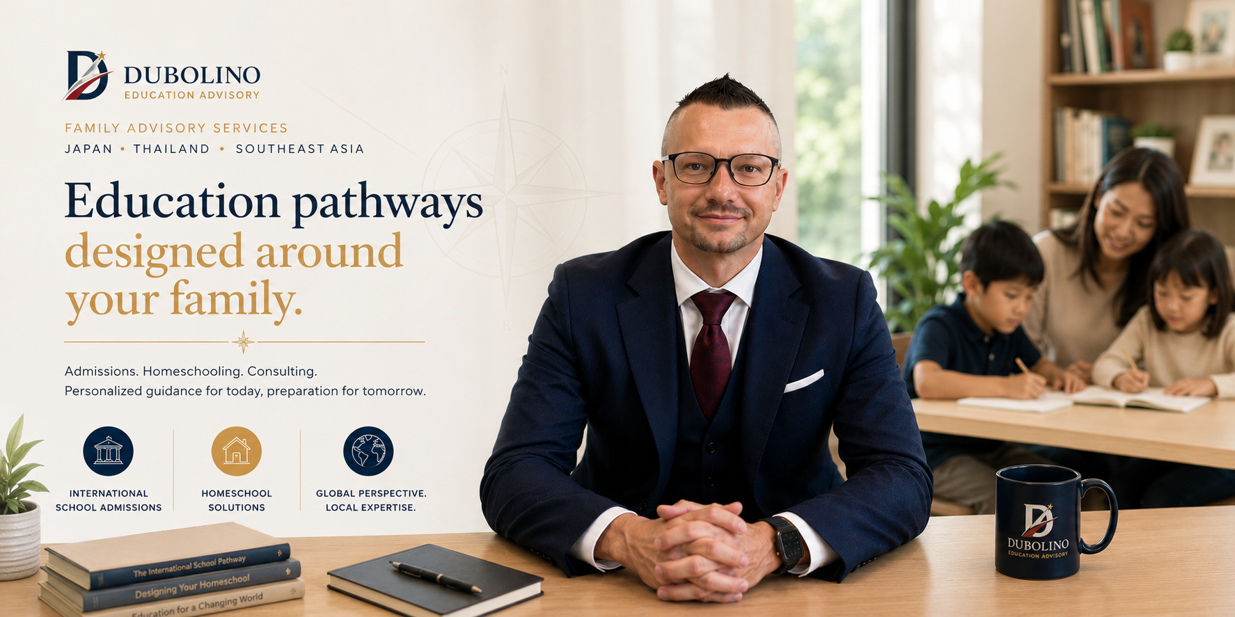 A professional man in glasses and a dark suit sitting at a desk with books, notebook, pen, and a branded mug, in a bright office with family and learning-themed branding on the wall.