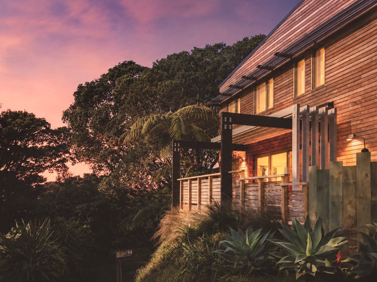 Adams Building architectural home with timber cladding surrounded by native bush at sunset in Fitzroy, New Plymouth.