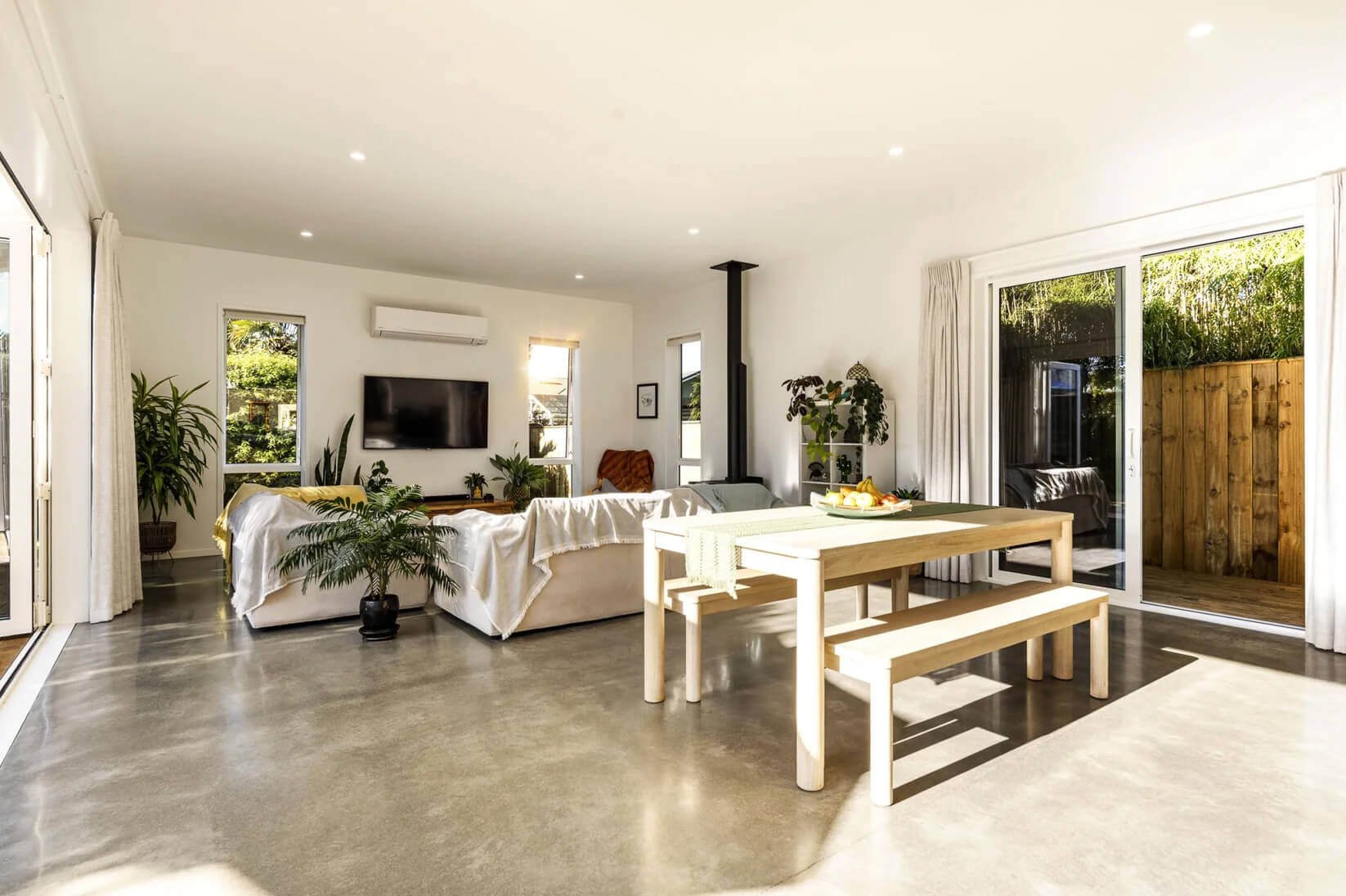 Adams Building open-plan dining and living area with wide folding doors opening onto timber decking in New Plymouth, Taranaki.