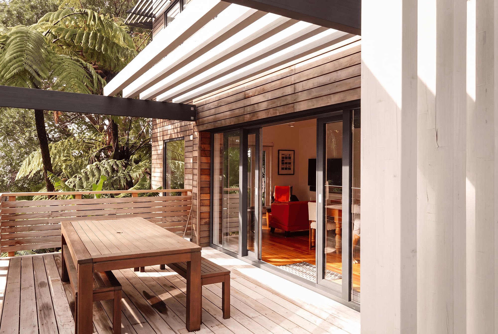 Timber-clad modern home with covered outdoor deck, large sliding doors and native greenery in Fitzroy, New Plymouth.