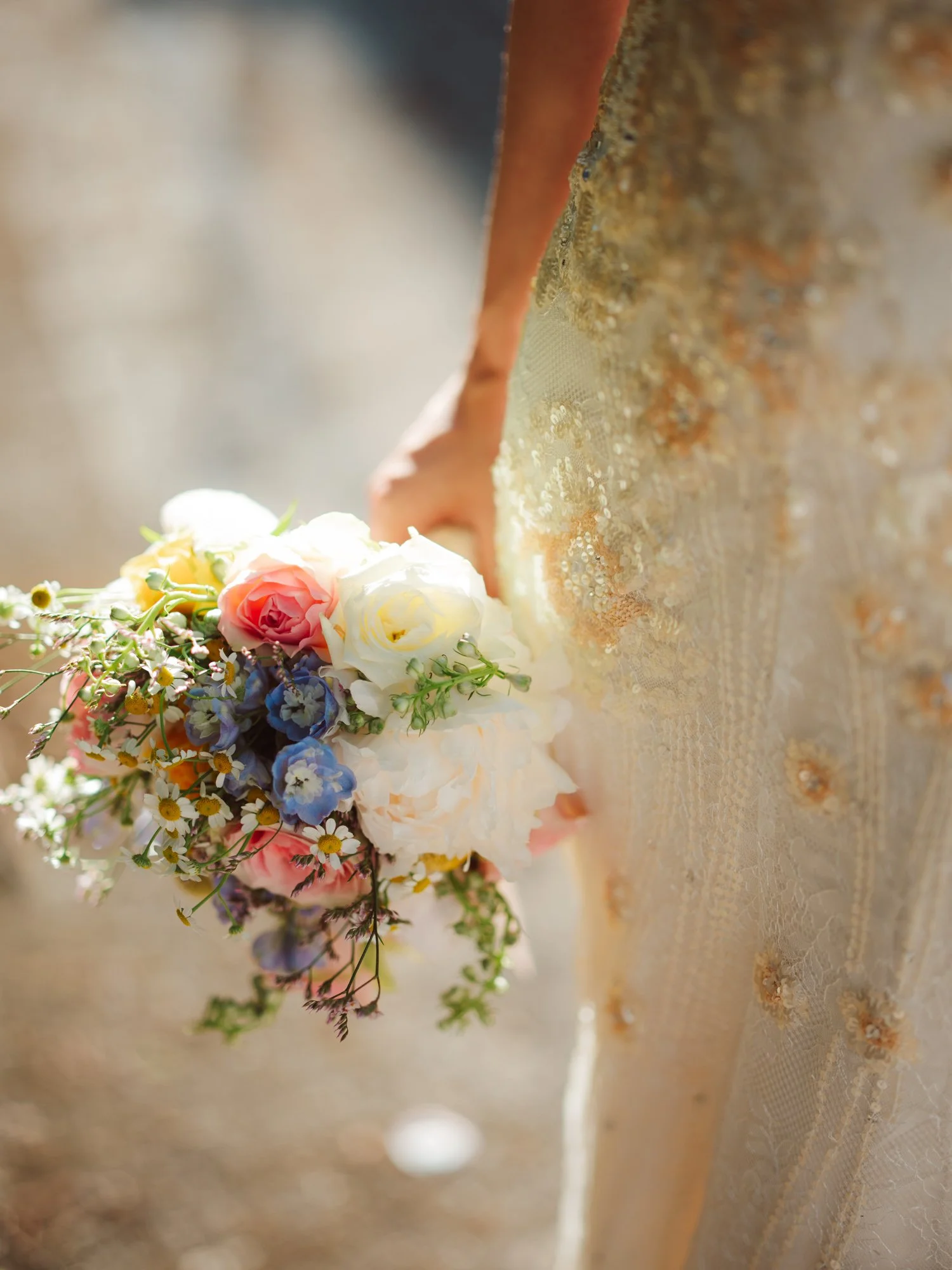 Primo piano del bouquet colorato con peonie e fiori di campo tenuto a lato dell'abito da sposa ricamato