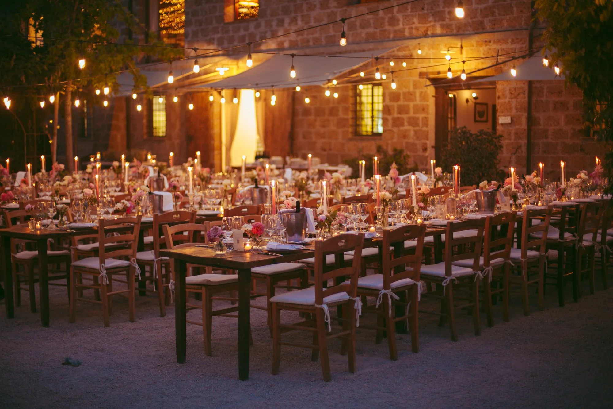 Tavoli in legno allestiti per la cena di nozze all'aperto sotto catene di luci suggestive nel cortile di Borgo di Tragliata