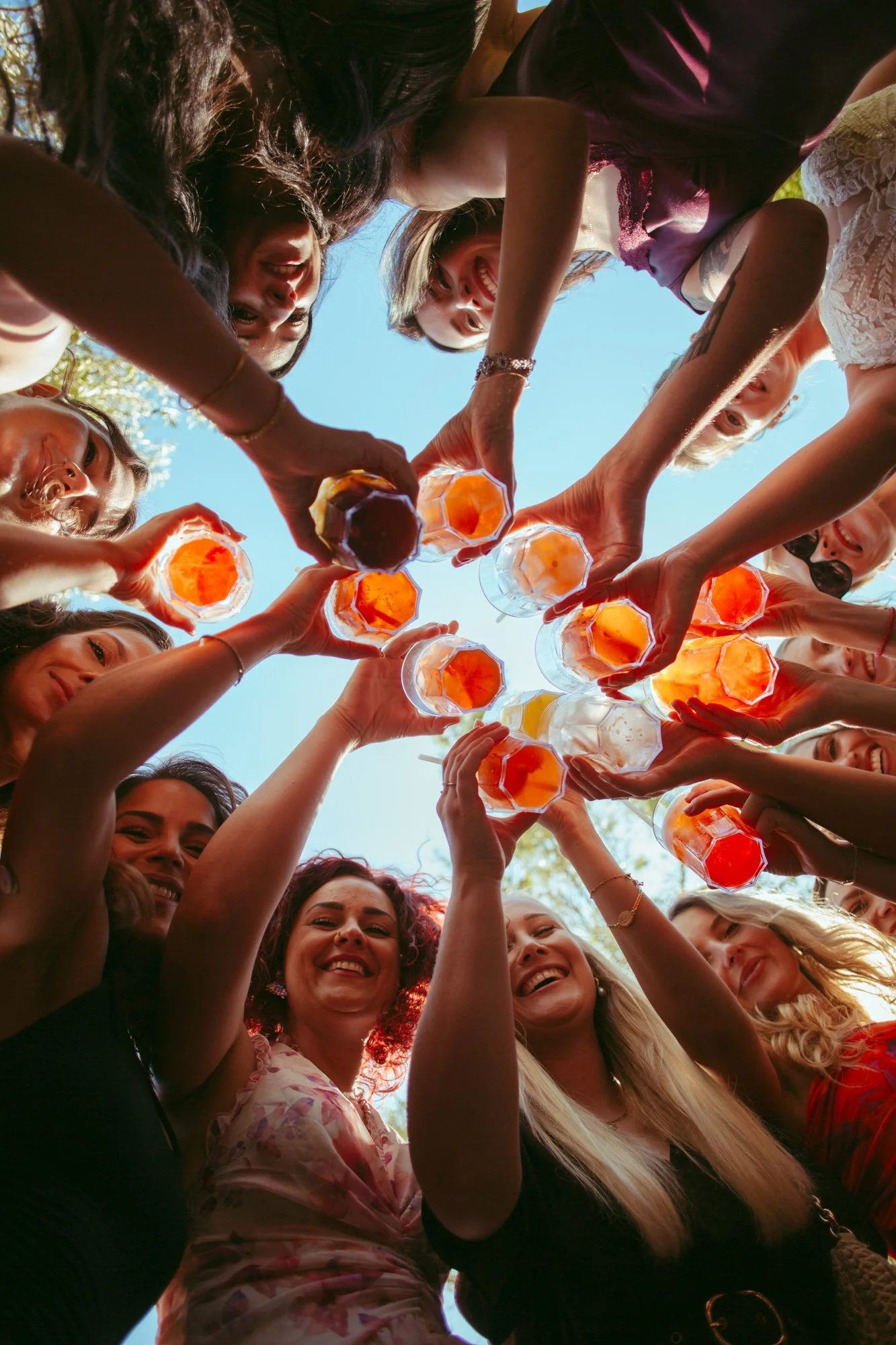 Prospettiva dal basso del brindisi di gruppo con i bicchieri di cocktail colorati e i volti sorridenti delle invitate e della sposa