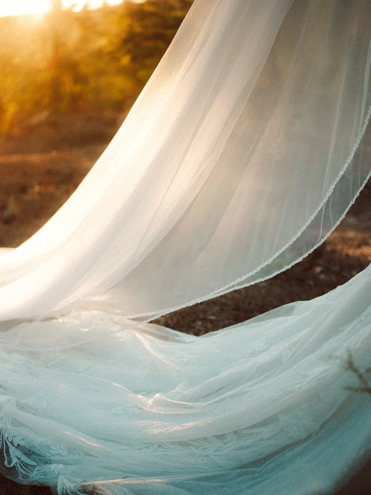 Dettaglio artistico del bordo ricamato del velo da sposa accarezzato dai raggi del sole al tramonto