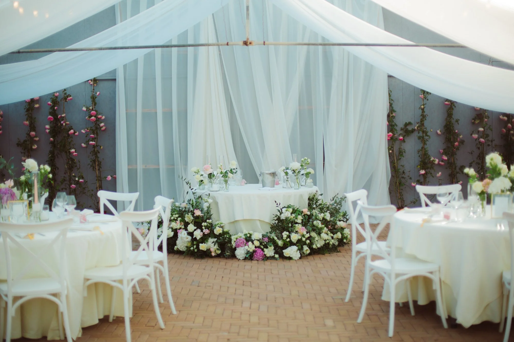Tavolo d'onore per gli sposi riccamente decorato con cascata di fiori alla base e drappeggi di tessuto bianco