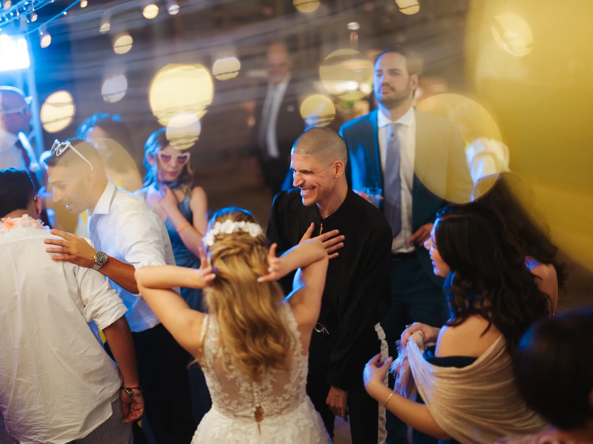 Gli ospiti e la sposa di spalle ballano divertiti insieme al centro della pista