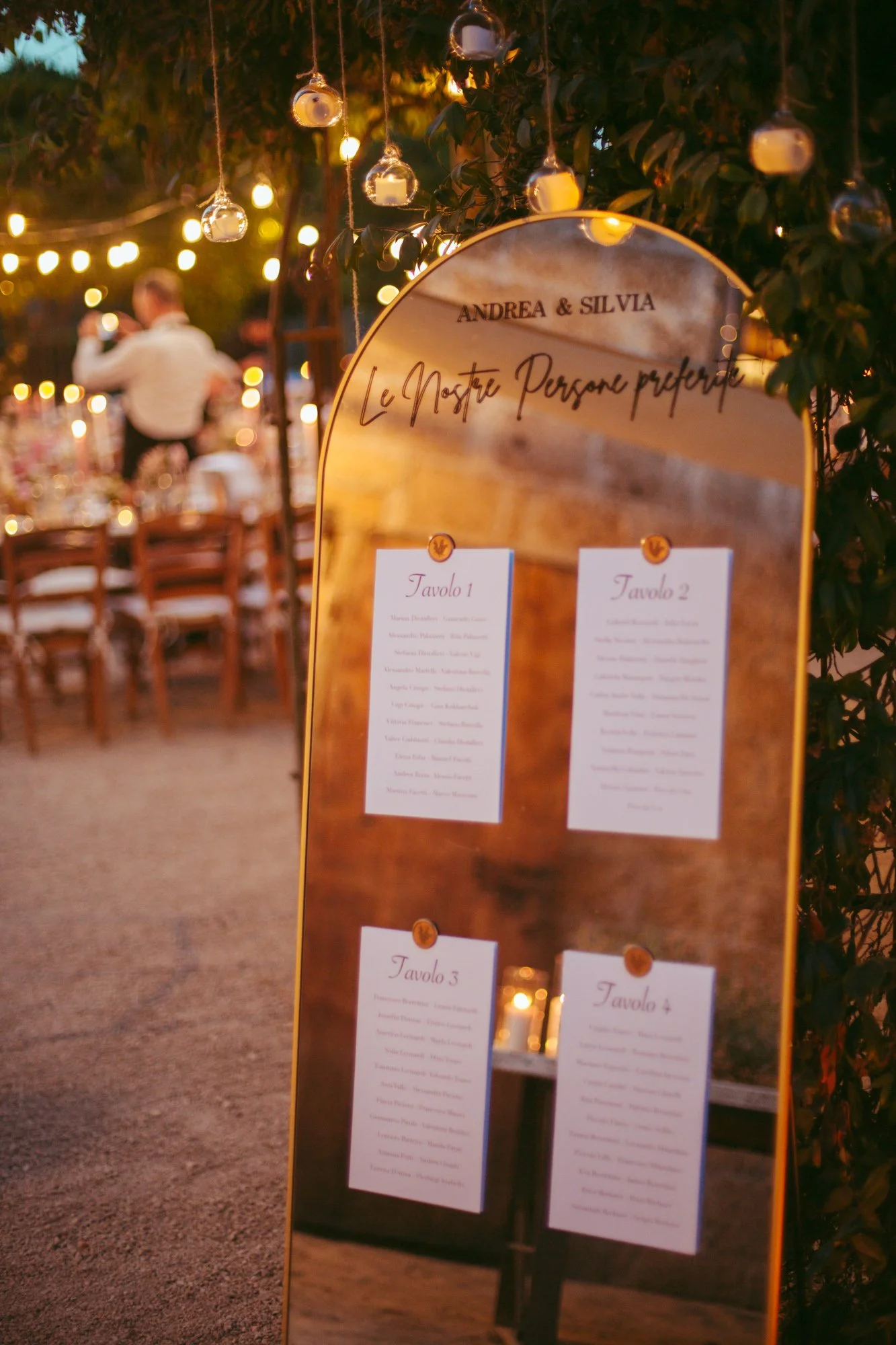 Elegante tableau de mariage a specchio curvo con la lista degli invitati e luci calde sullo sfondo a Borgo di Tragliata