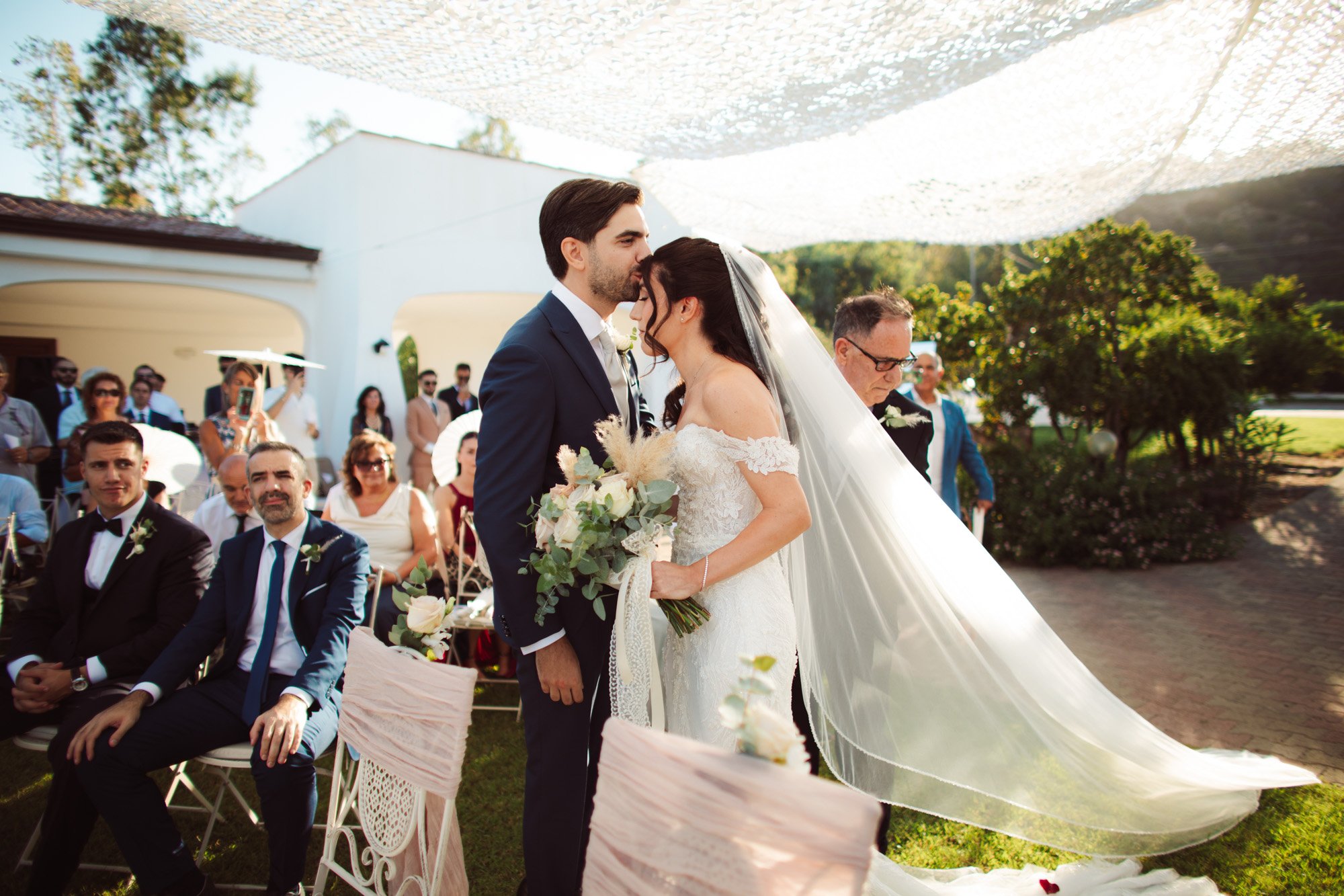 Lo sposo bacia teneramente la fronte della sposa sotto la copertura in pizzo durante la cerimonia nuziale.