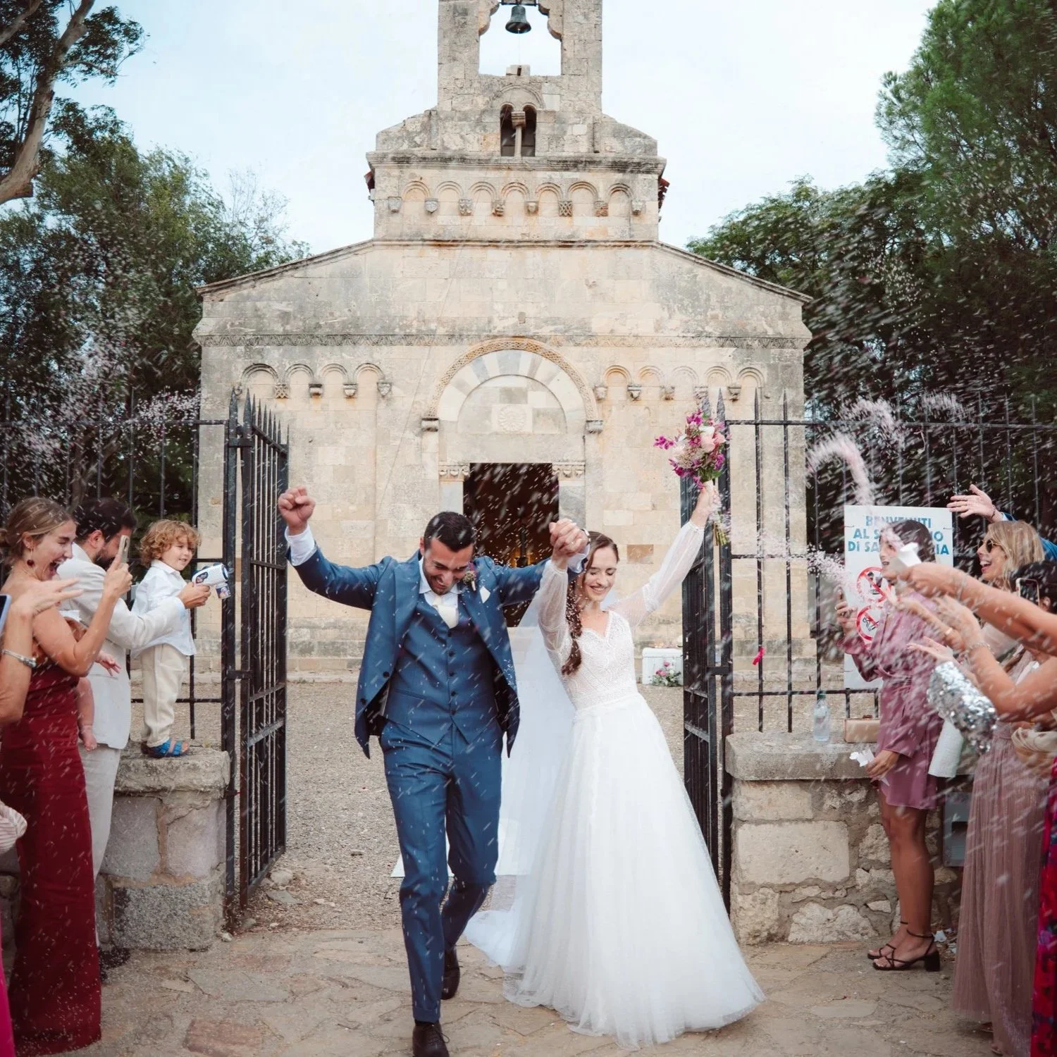 Una coppia di sposi felici esce da una chiesa, circondata da amici e parenti che lanciando riso, celebrano il matrimonio.