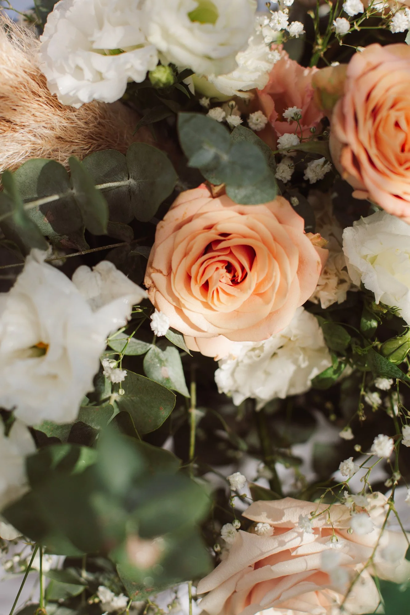 Primo piano ravvicinato di una raffinata composizione floreale con rose color pesca, eucalipto e fiori bianchi.