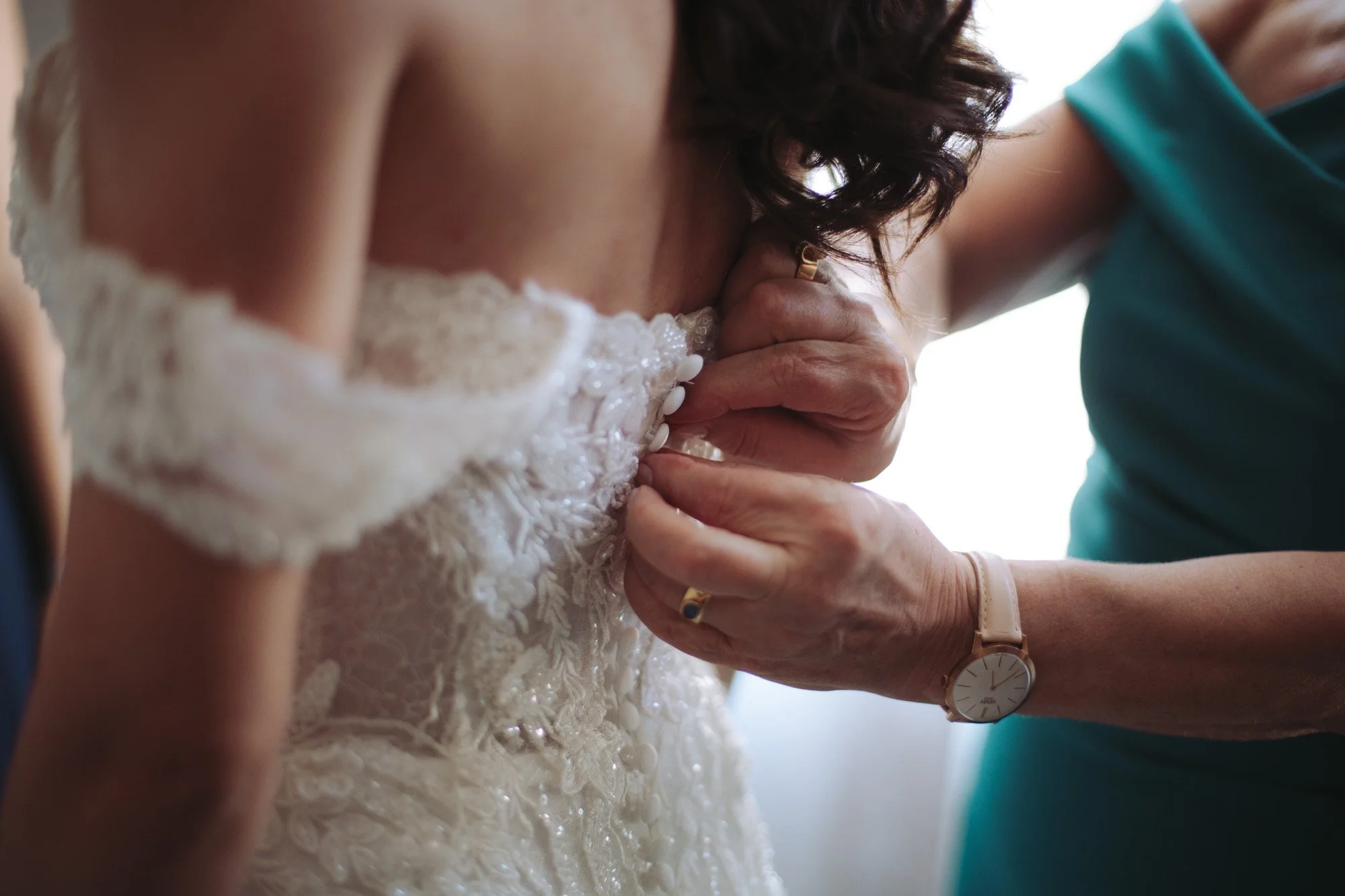 Primo piano ravvicinato delle mani che bottonano l'abito da sposa in pizzo lavorato a mano.