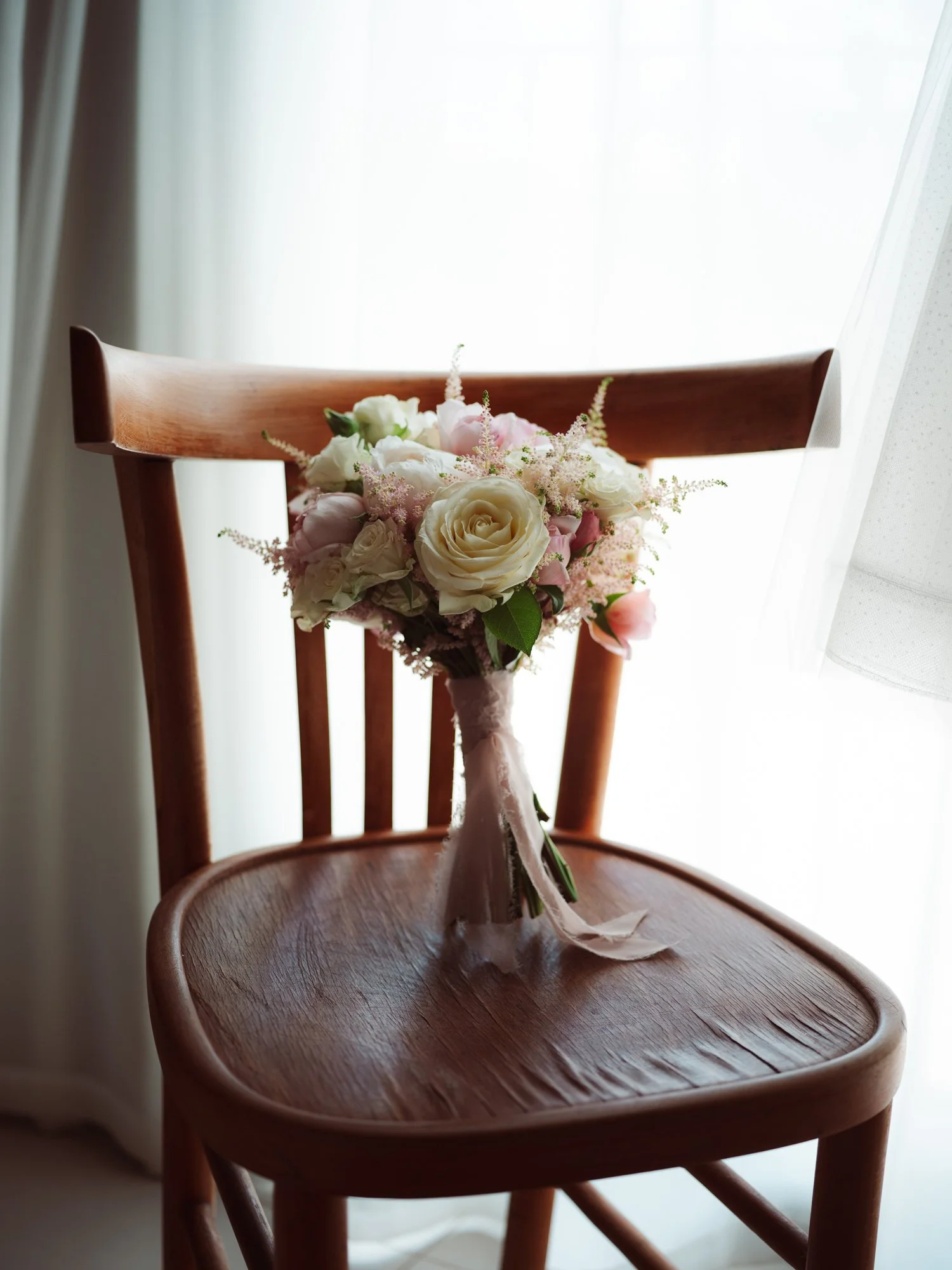 Bouquet da sposa con rose bianche e rosate appoggiato su una sedia in legno d'epoca