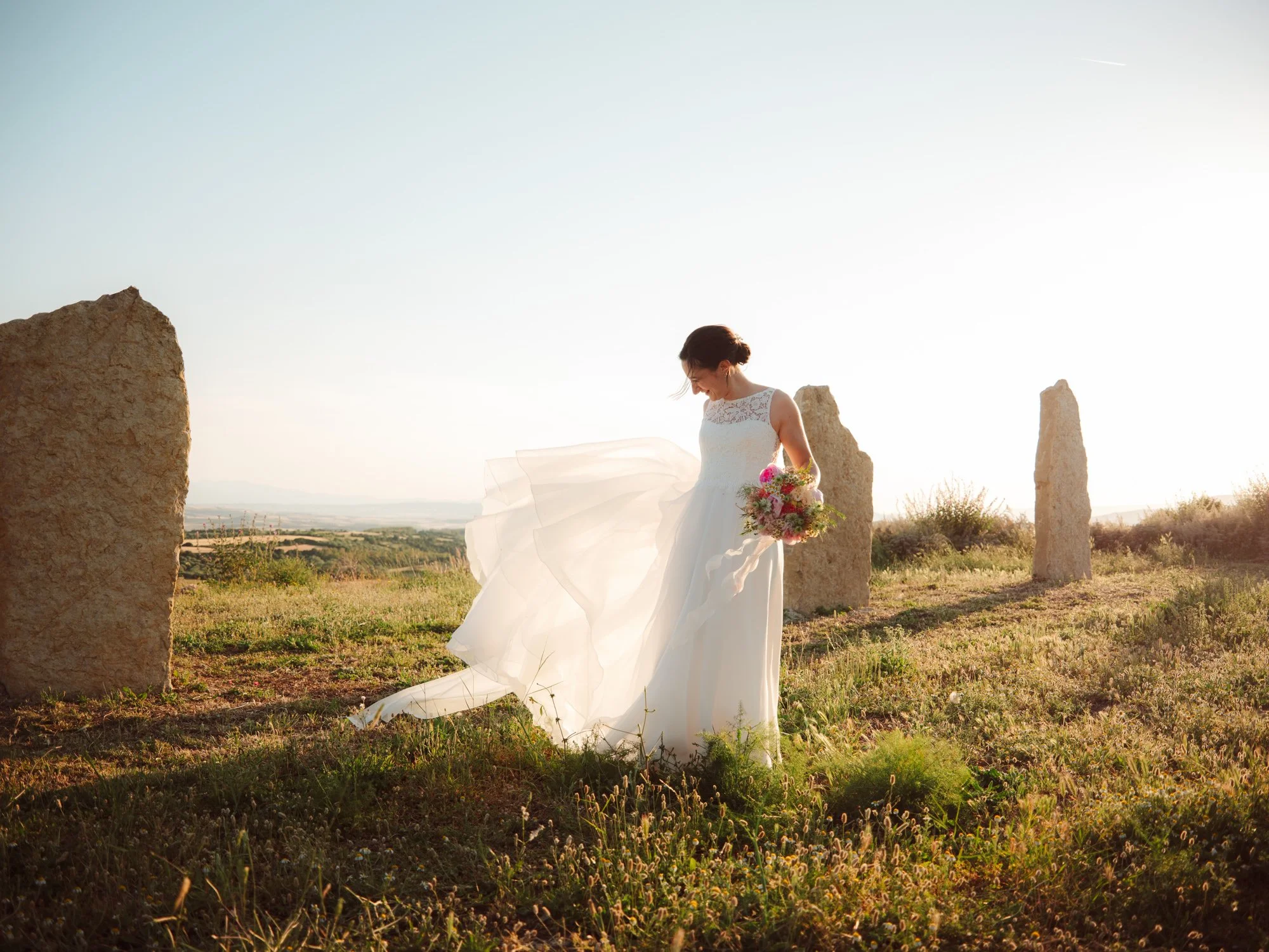 Ritratto della sposa sorridente con l'abito mosso dal vento al tramonto