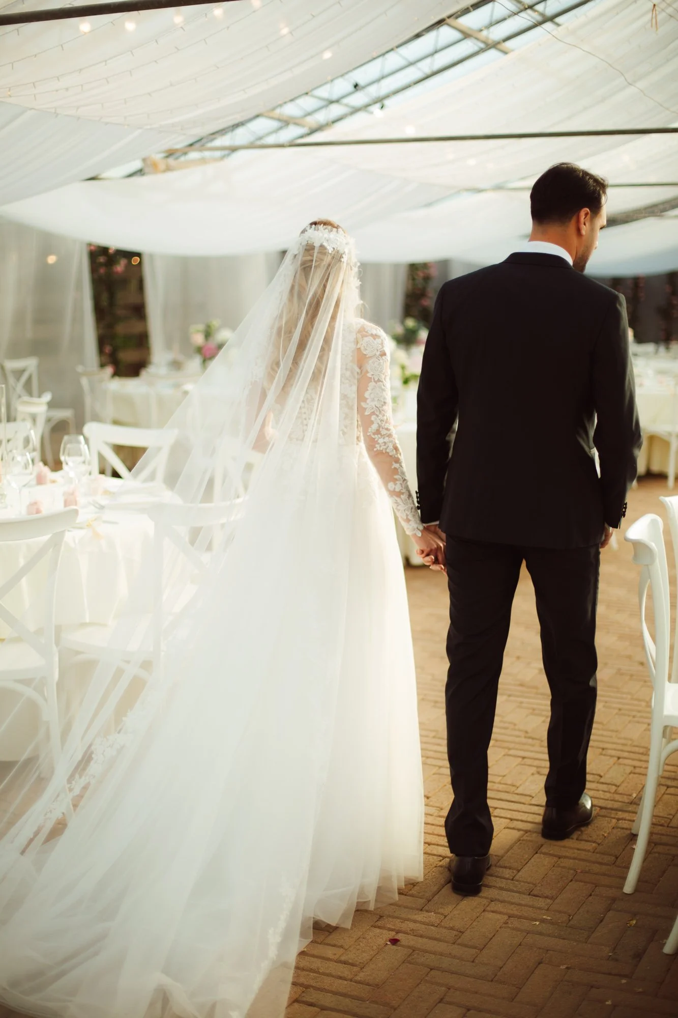 Sposa e sposo si tengono per mano camminando tra i tavoli allestiti all'interno della serra decorata