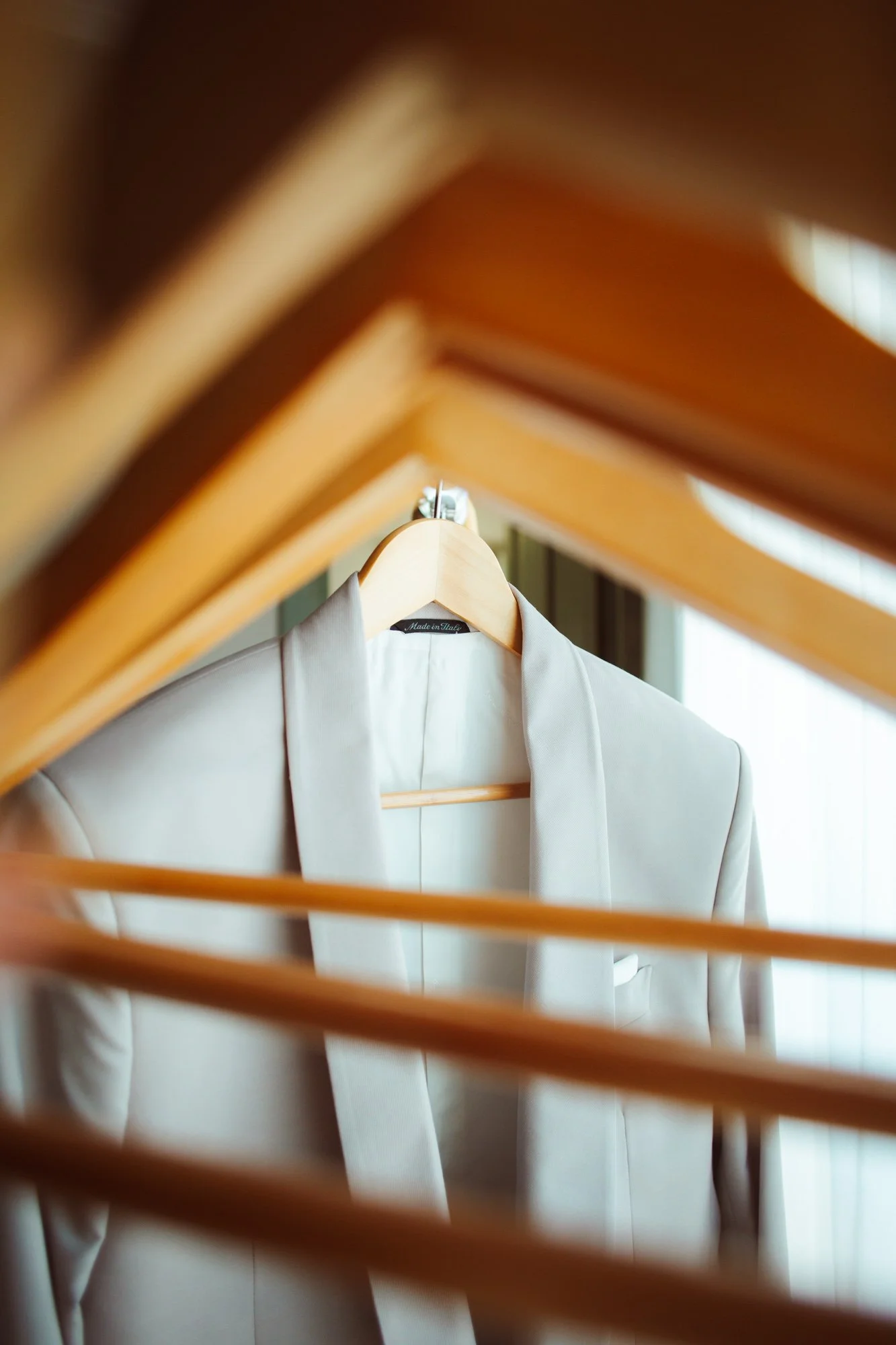 Inquadratura artistica della giacca sartoriale dello sposo in tonalità beige chiaro appesa a una gruccia di legno