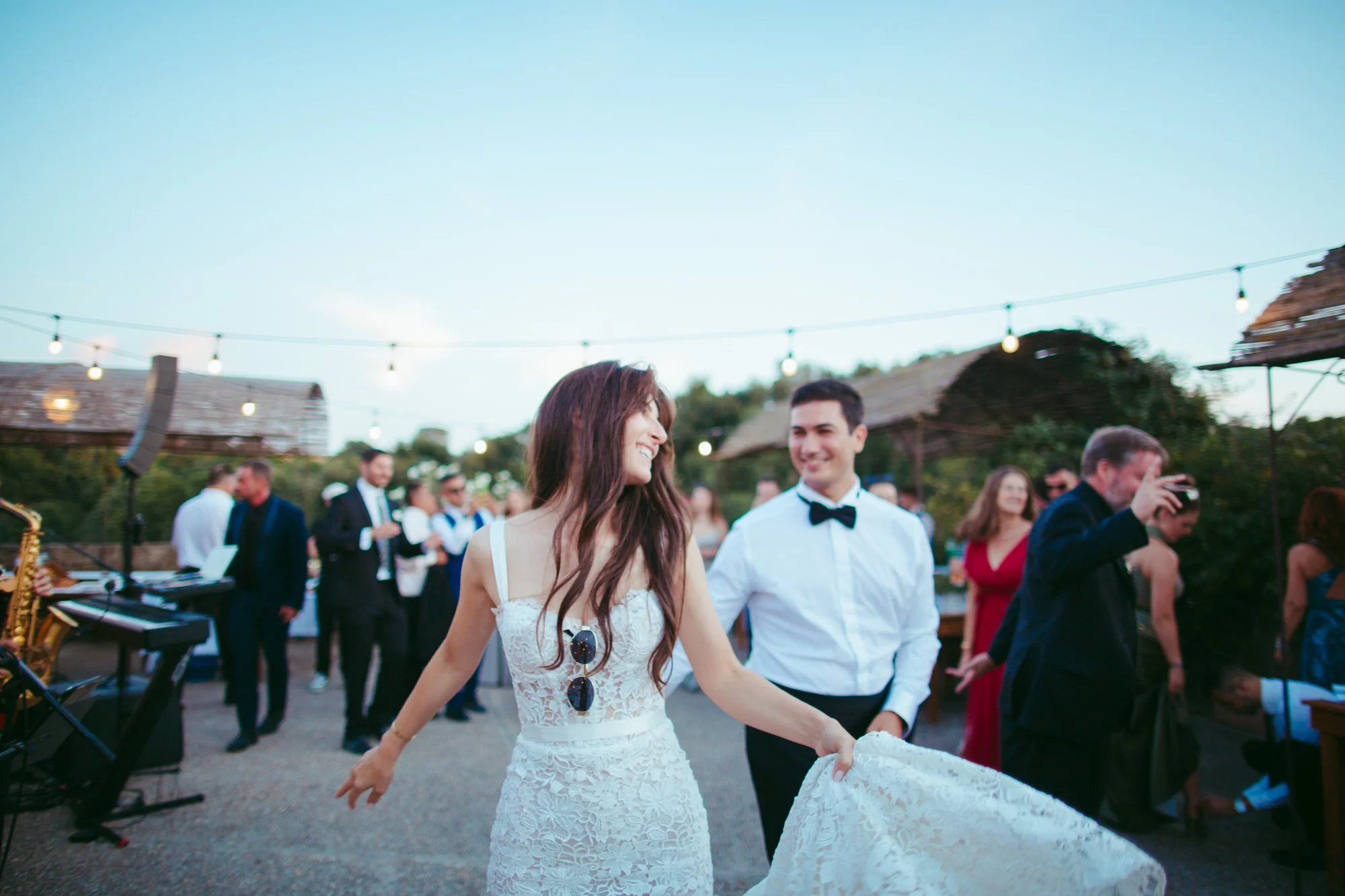 La sposa sorridente tiene il vestito mentre balla all'aperto insieme allo sposo e agli invitati nella location di Tragliata
