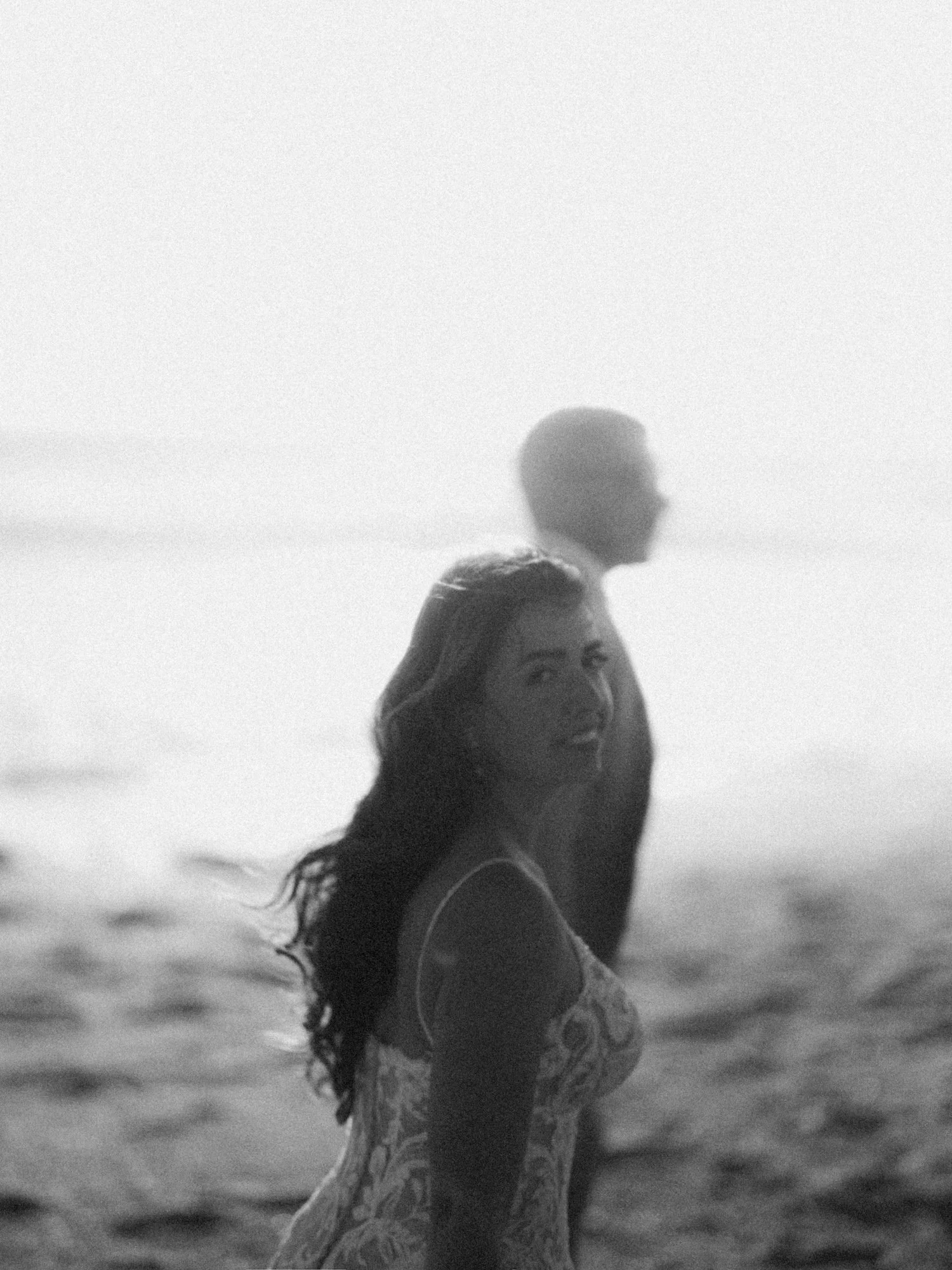 Una sposa con i capelli lunghi e mossi, che sorride mentre si trova in riva al mare, vestita con un abito leggero.