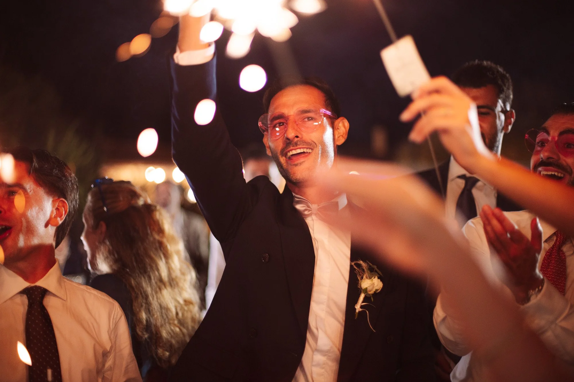 Un invitato felice con occhiali da sole festeggia con le classiche scintille luminose durante la festa di nozze