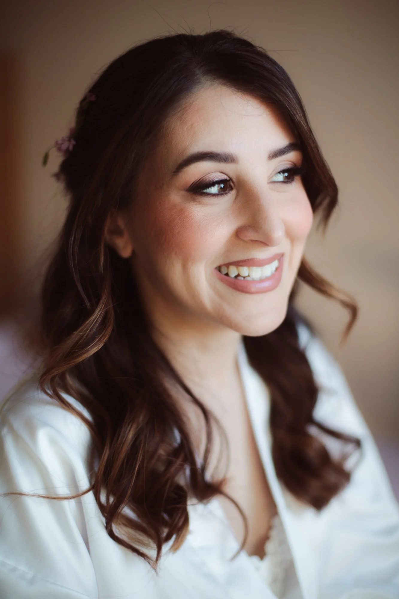 Primo piano sorridente della sposa con trucco luminoso sui toni caldi, rossetto rosato e capelli semiraccolti