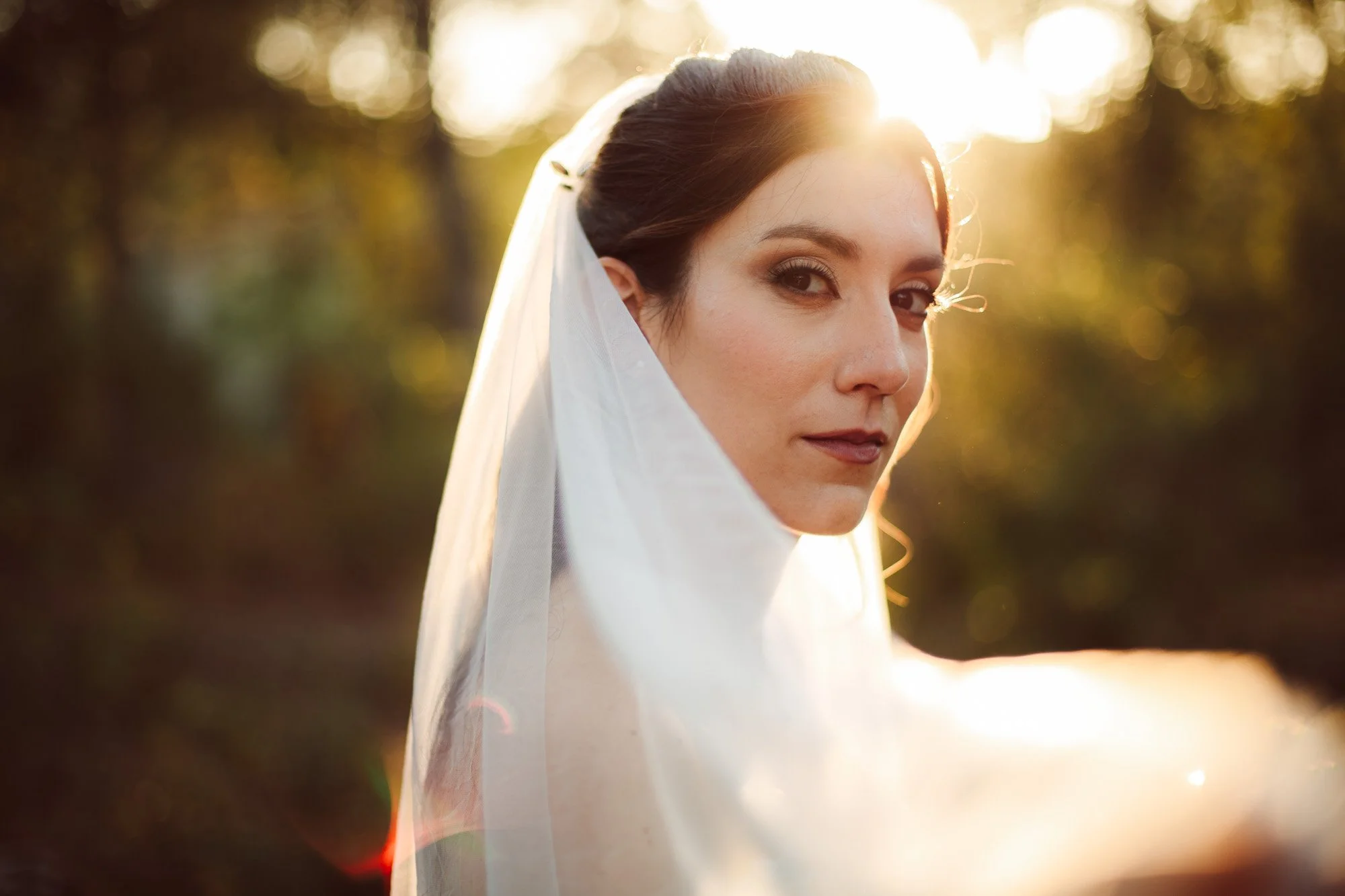 Primo piano ravvicinato della sposa incorniciata dal velo con un raffinato effetto lens flare al tramonto.