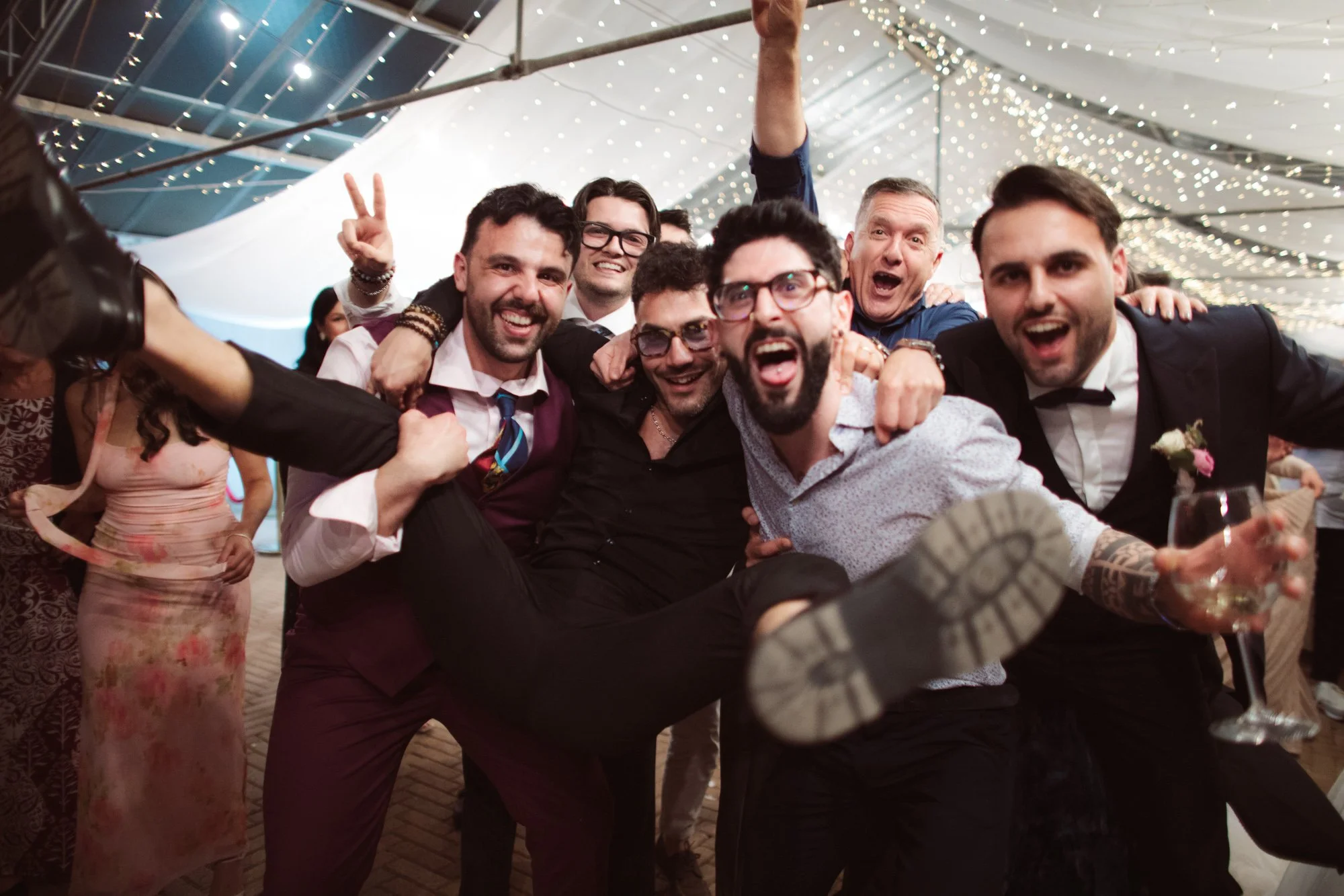 Lo sposo e un gruppo di amici afferrano e sollevano un invitato in modo goliardico e festoso urlando di gioia