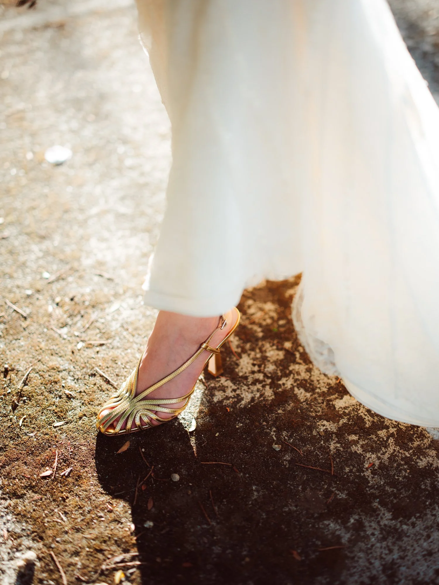 Primo piano del piede della sposa che indossa un elegante sandalo dorato con listini sottili mentre cammina