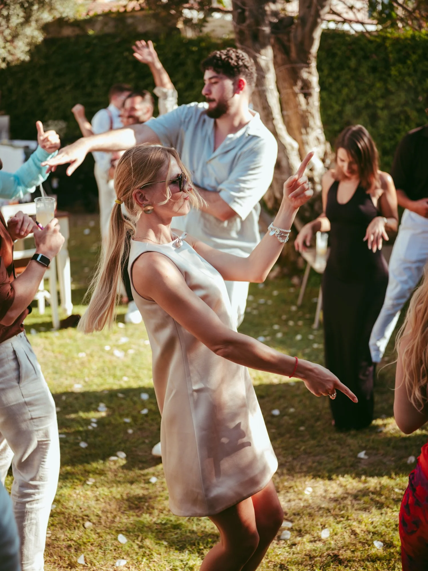 Invitata bionda con abito chiaro e occhiali da sole balla a ritmo di musica nel giardino della location