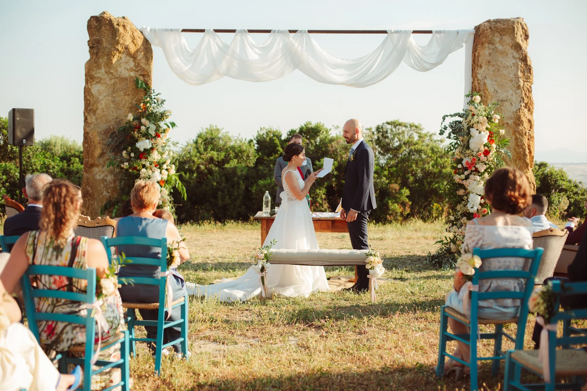 Vista dagli ospiti del rito simbolico di matrimonio tra le pietre sotto l'arco floreale in Sardegna
