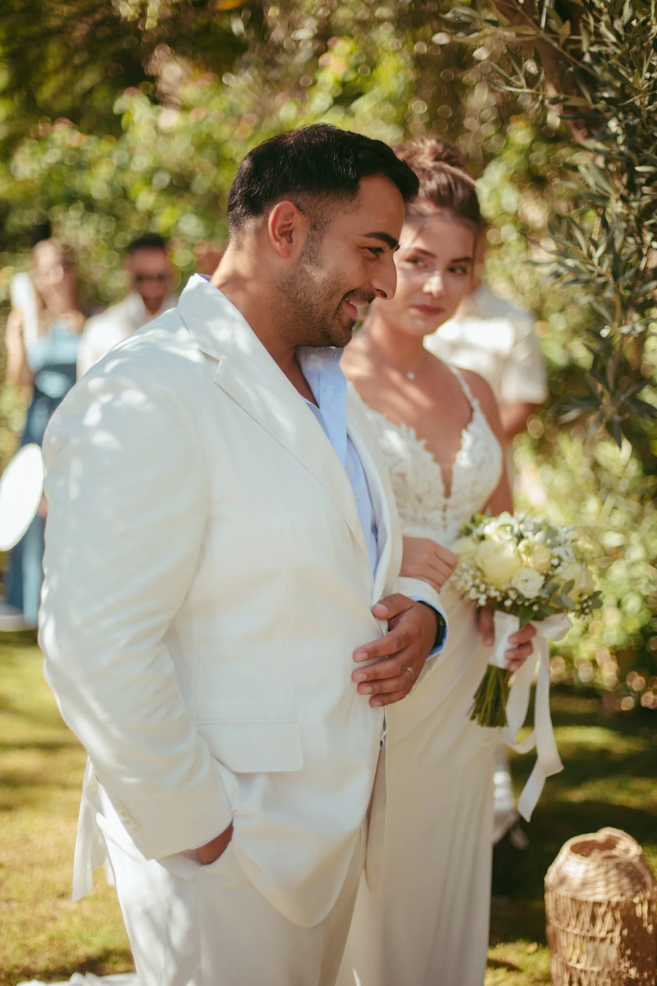 Lo sposo in abito chiaro sorride mentre la sposa lo guarda intensamente durante la cerimonia all'aperto