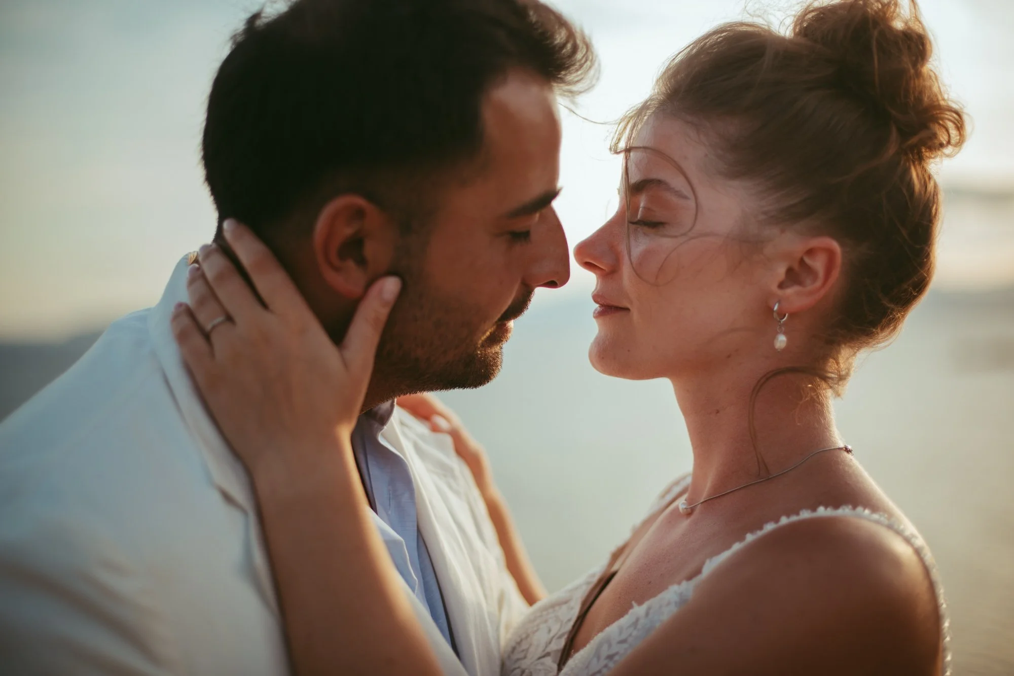 Primo piano intimo della sposa che accarezza il viso dello sposo con la luce calda del tramonto
