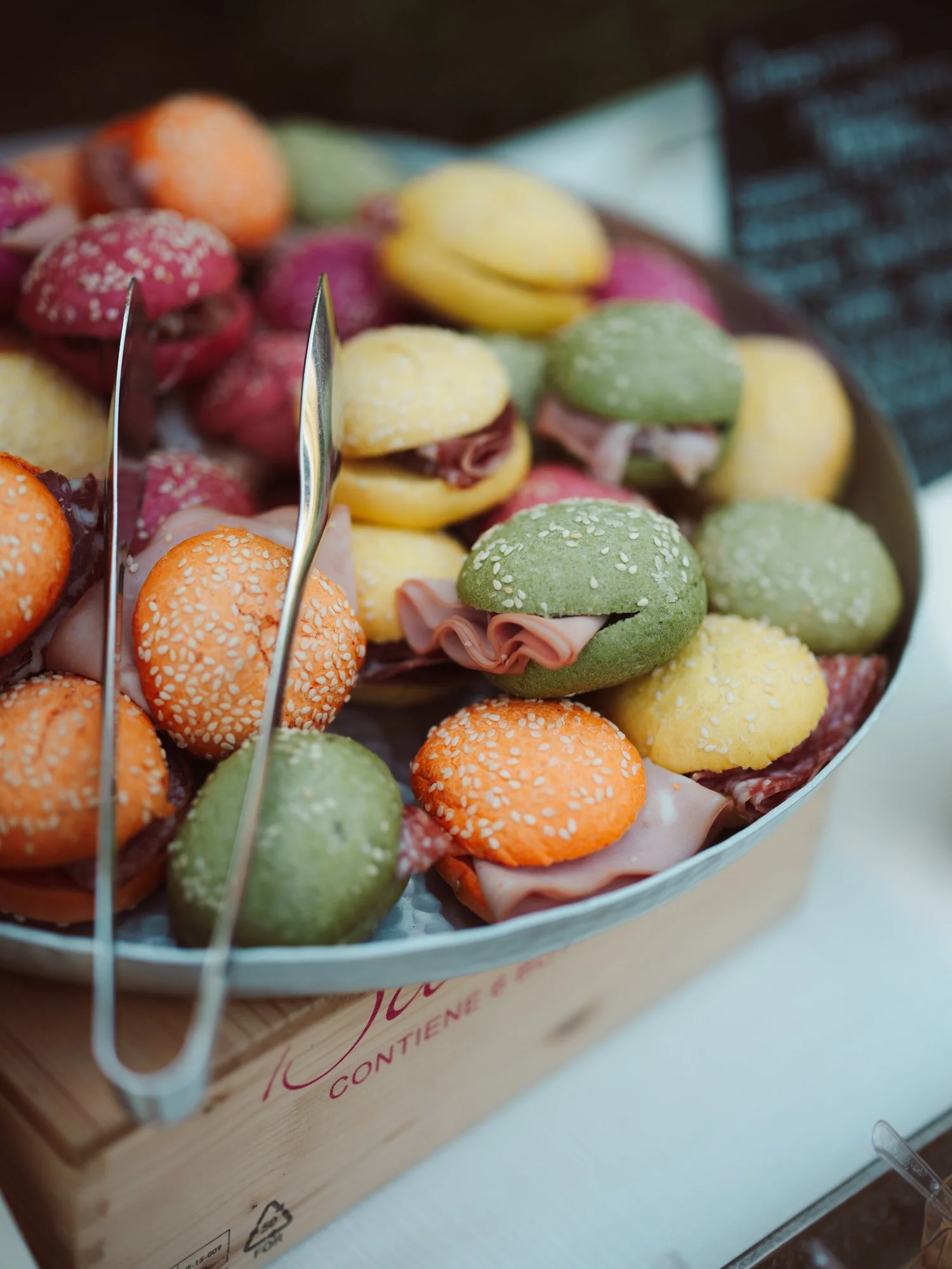 Vassoio pieno di sfiziosi mini panini gourmet colorati di verde, arancione e giallo farciti con affettati