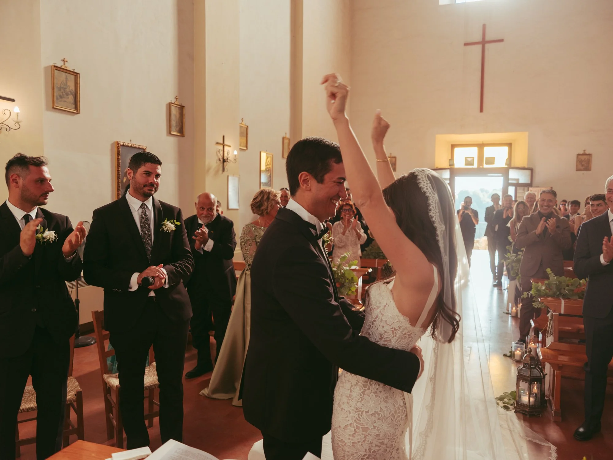 La sposa alza le braccia al cielo festeggiando insieme allo sposo subito dopo la fine della cerimonia di nozze