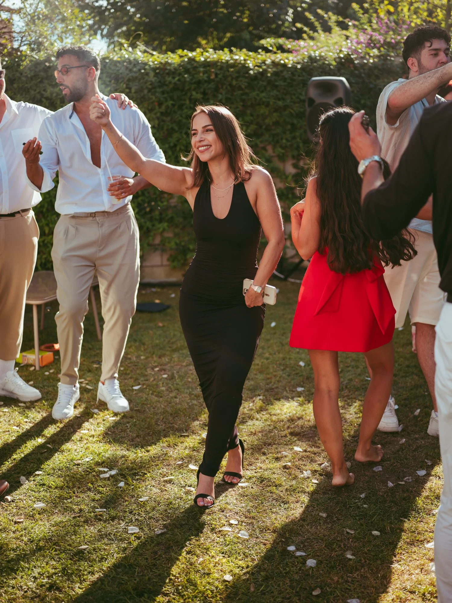 Invitata elegante in abito nero lungo balla sorridente sul prato durante il party