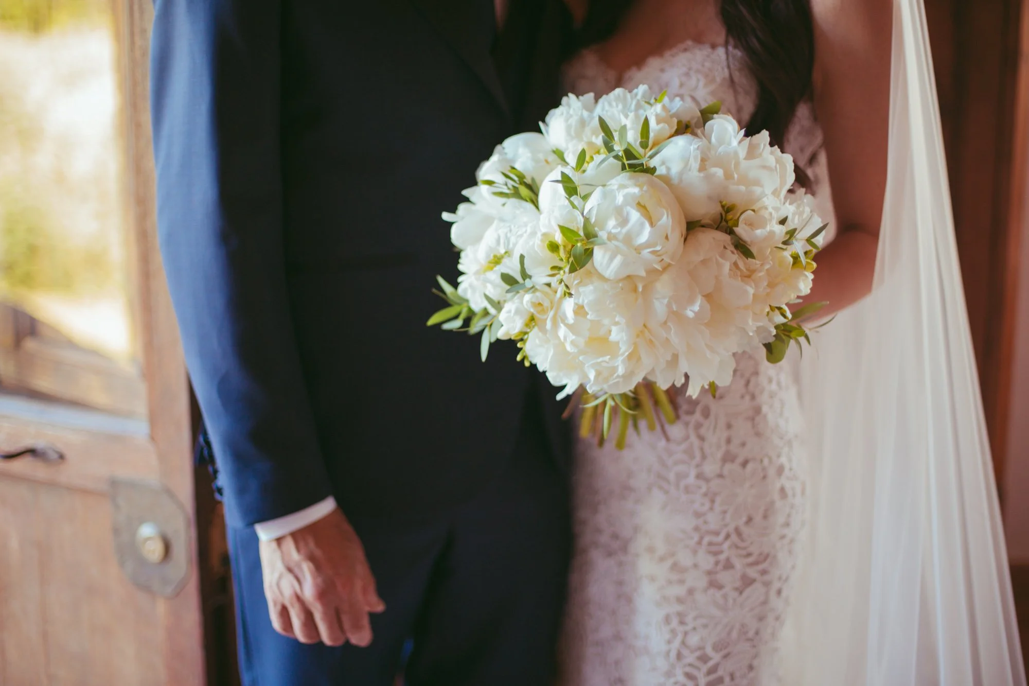 Dettaglio in primo piano del bouquet da sposa di peonie bianche tenuto dalla sposa accanto al papà