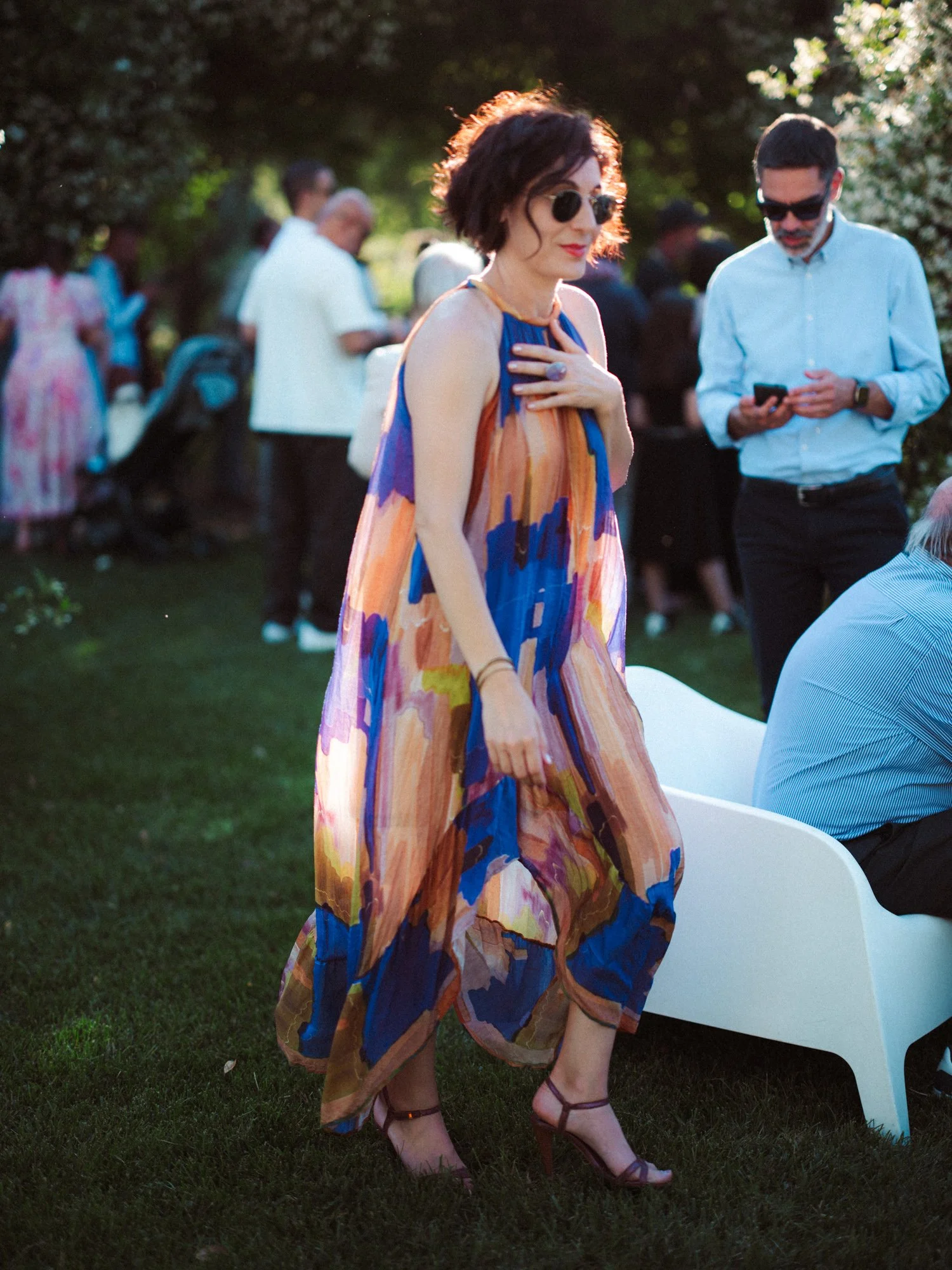 Invitata elegante in abito lungo e leggero a fantasia colorata con occhiali da sole cammina nel giardino durante l'aperitivo