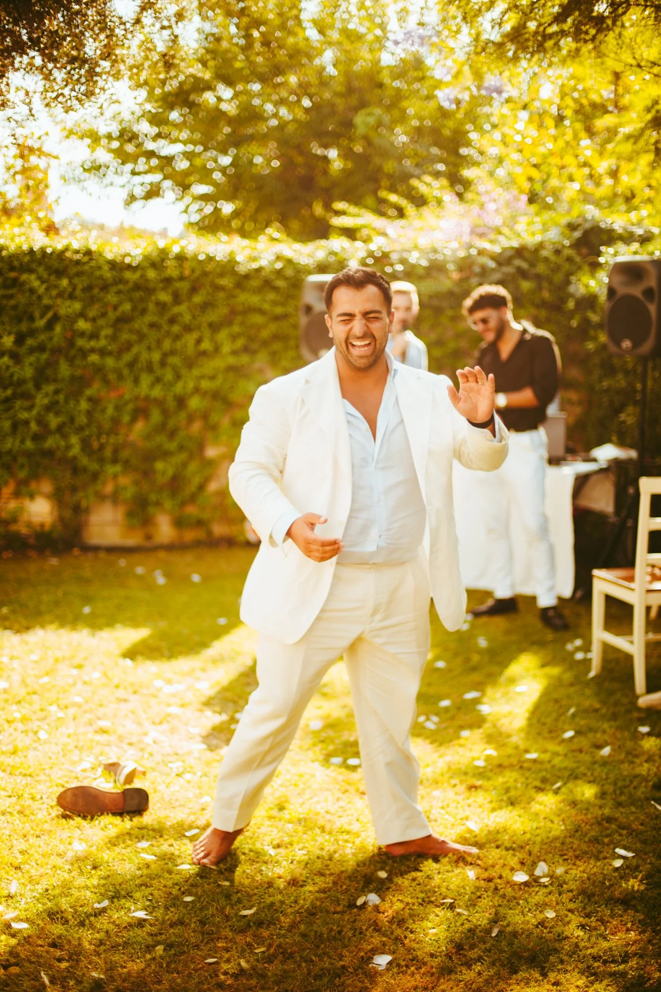 Lo sposo in abito bianco balla felicissimo a piedi nudi sul prato durante il party all'aperto