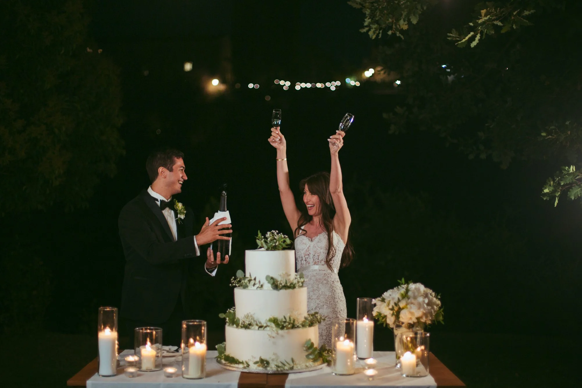 La sposa alza i calici per brindare festosamente accanto allo sposo e alla torta nuziale durante il ricevimento a Tragliata