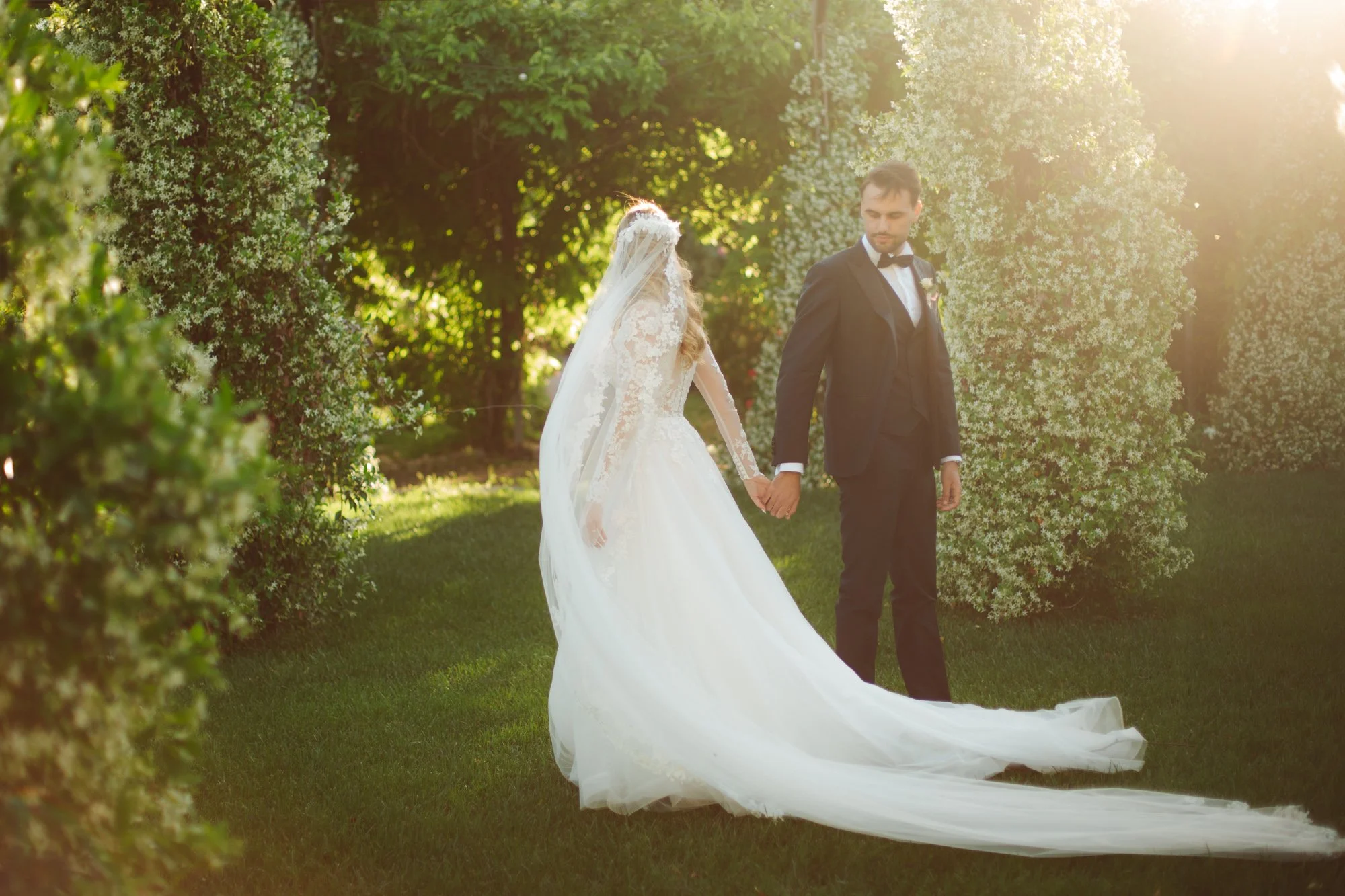 La sposa vista da dietro trascina lo strascico dell'abito mentre tiene la mano dello sposo che si volta a guardarla