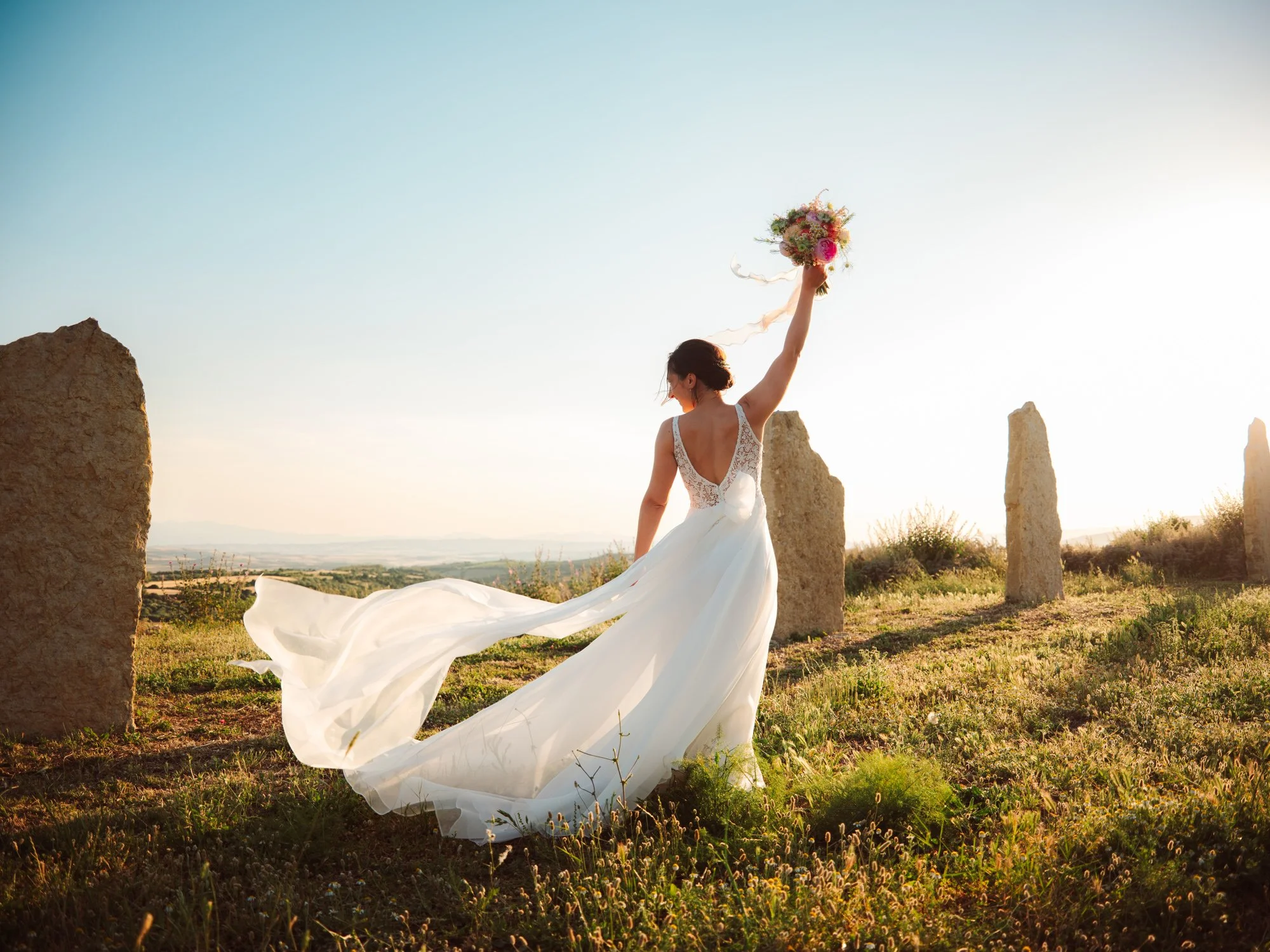 Sposa che solleva il bouquet al tramonto tra i menhir in Sardegna