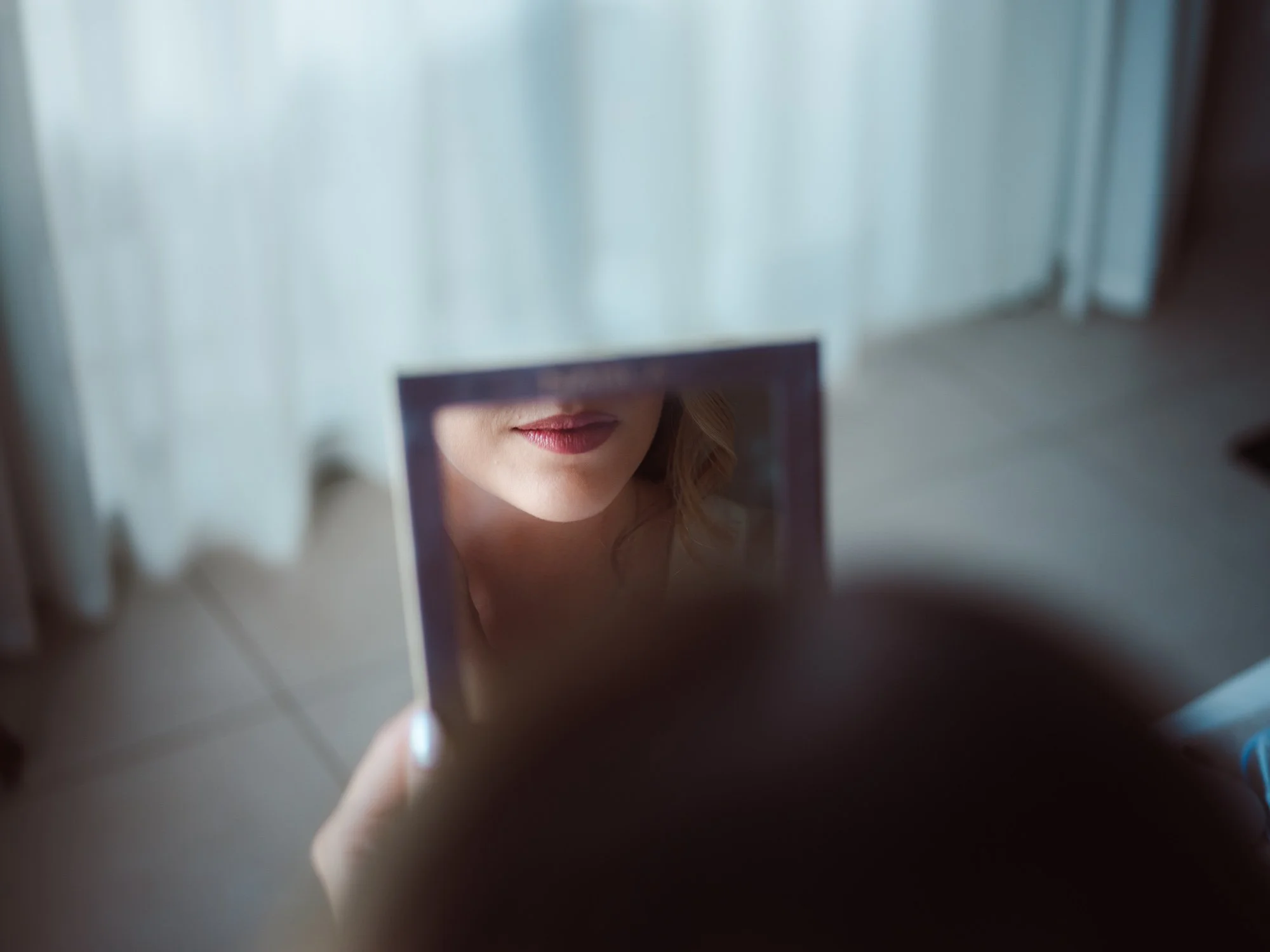 Dettaglio del riflesso delle labbra della sposa con rossetto rosato all'interno di un piccolo specchio da palette